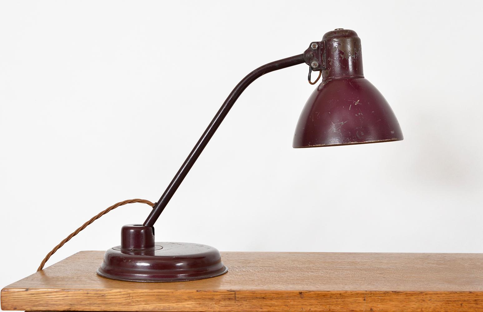 A lovely patinated articulated desk lamp in original burgundy/aubergine coloured paint. Sat on a metal round stepped base, which is weighted, allowing the curved brass rod arm to be manoeuvred forward and back, whilst the lamp shade pivots on a ball