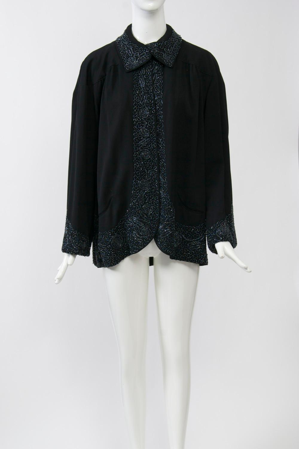 1940s black wool jacket with beaded trim on collar, cuffs, and border. The intricate beaded design follows the curve of the hem, widening as it descends, and features a scalloped design throughout the swing back. A set-in yoke follows the same shape
