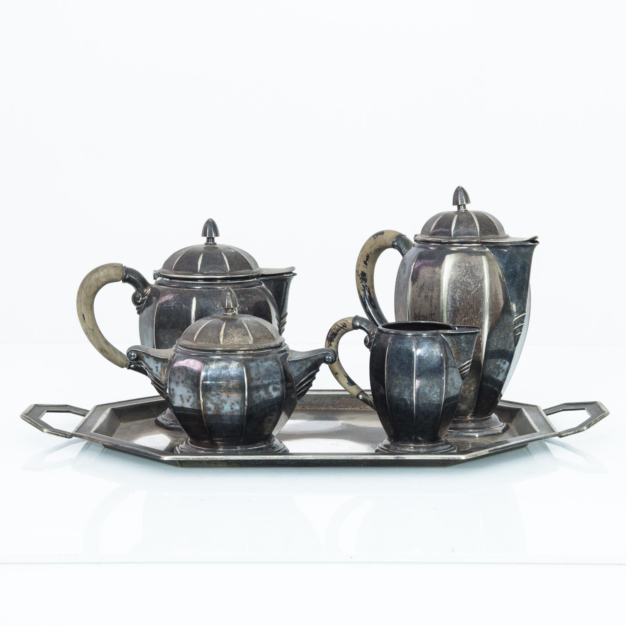 A five piece metal coffee set from Belgium, produced circa 1940. Old word nobility meets angular Art Deco in this coffee set featuring a coffee pot, teapot, sugar bowl, and milk pitcher, all placed upon a metal tray. A set so stunning, it strikes