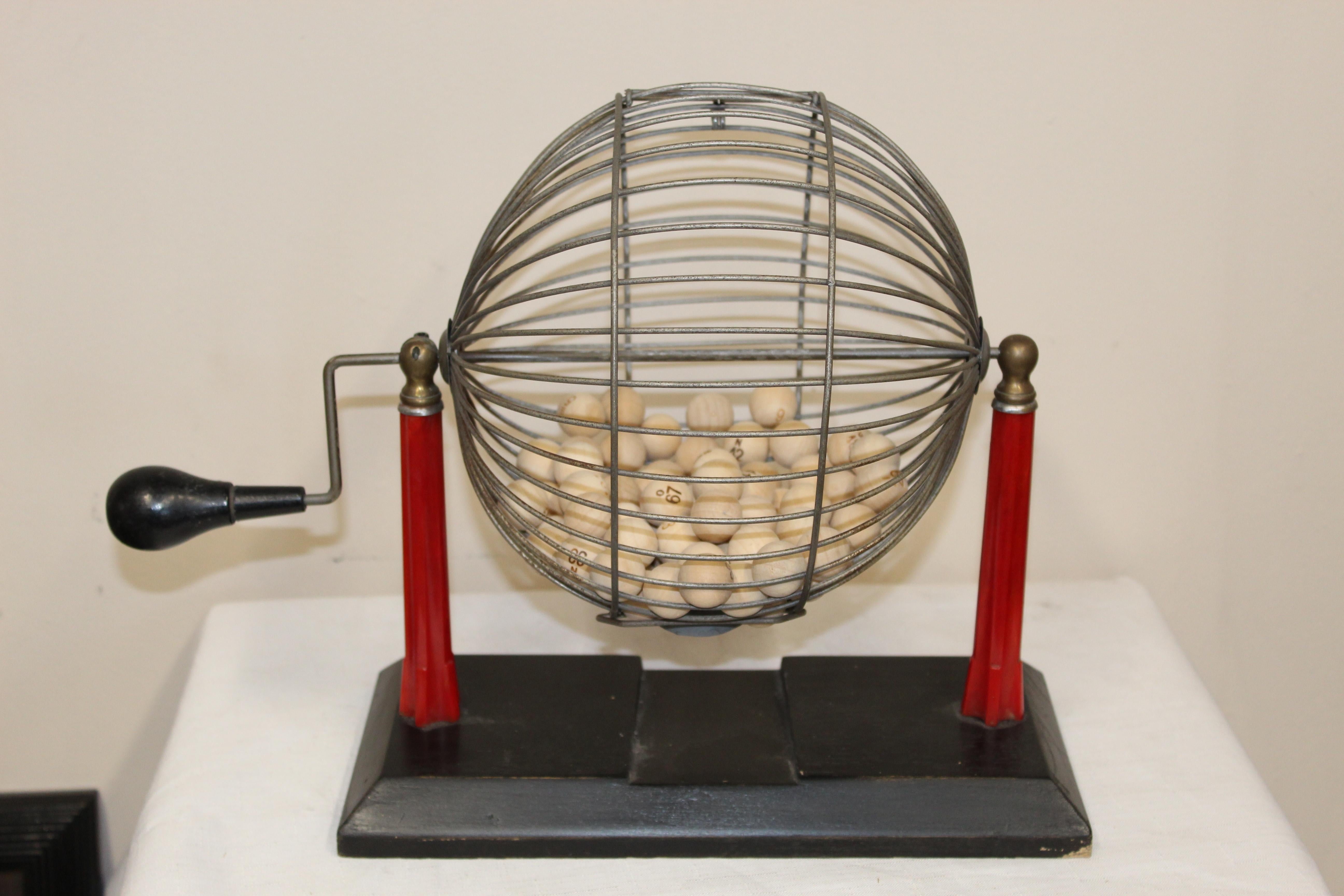 Bingo cage with bakelite red stand and an handle. Original condition, some small imperfections but over all in clean condition. Wood balls are included and numbered.