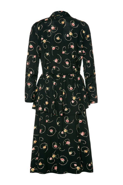 This desirable original unlabelled 1940’s day dress in black rayon with a pretty pink rose print is an incredibly versatile piece and can be dressed up or down.    It features long sleeves, a shirt collar, peplum detail from the waist and button up