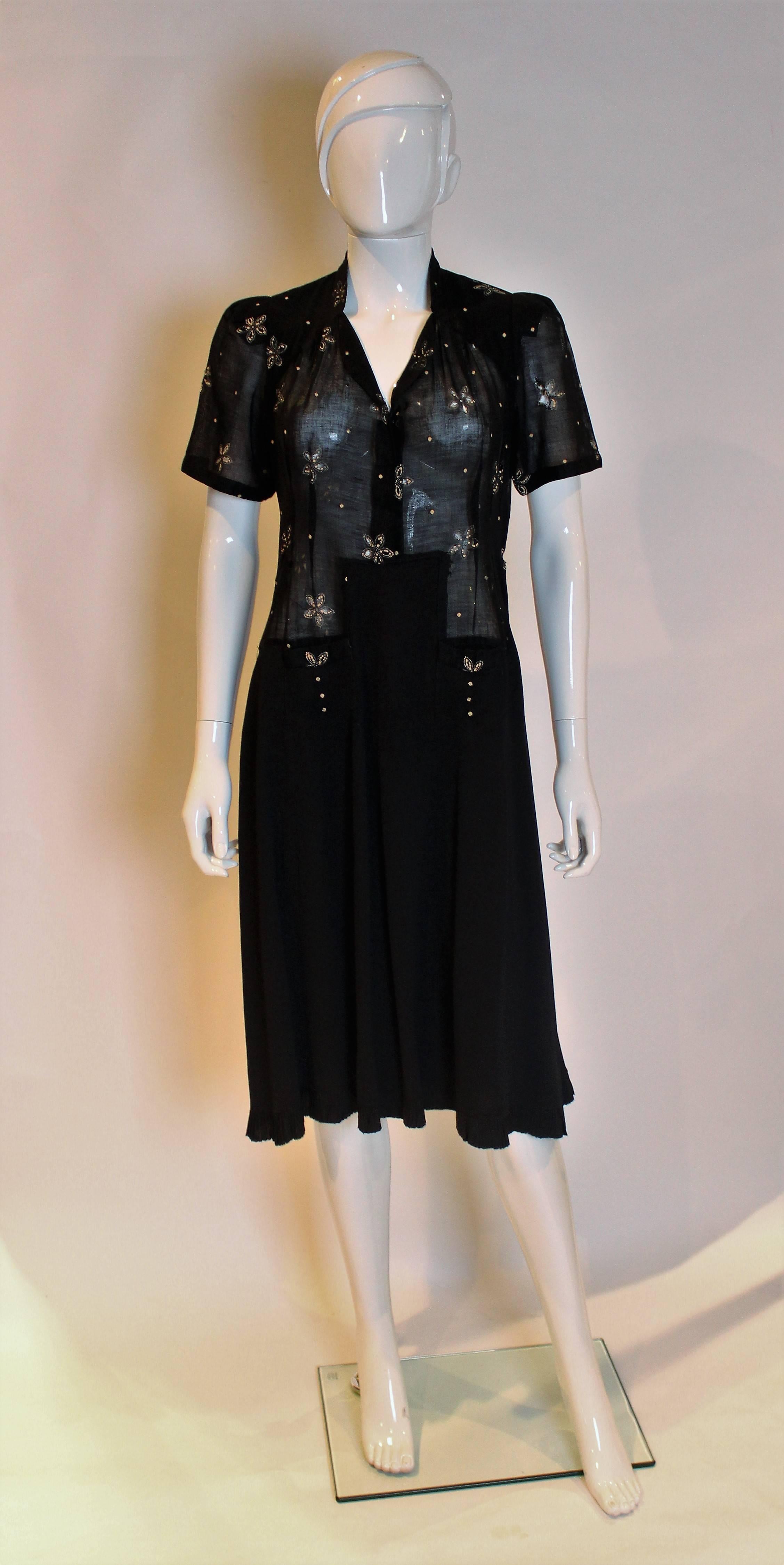 A chic dress from the 1940s. The bodice is a cotton net like fabric with hand painted flowers and cut out petals. The dress has a sweet hear neckline and short sleeves,and it opens at the front and side with hooks and eyes. The skirt is black crepe