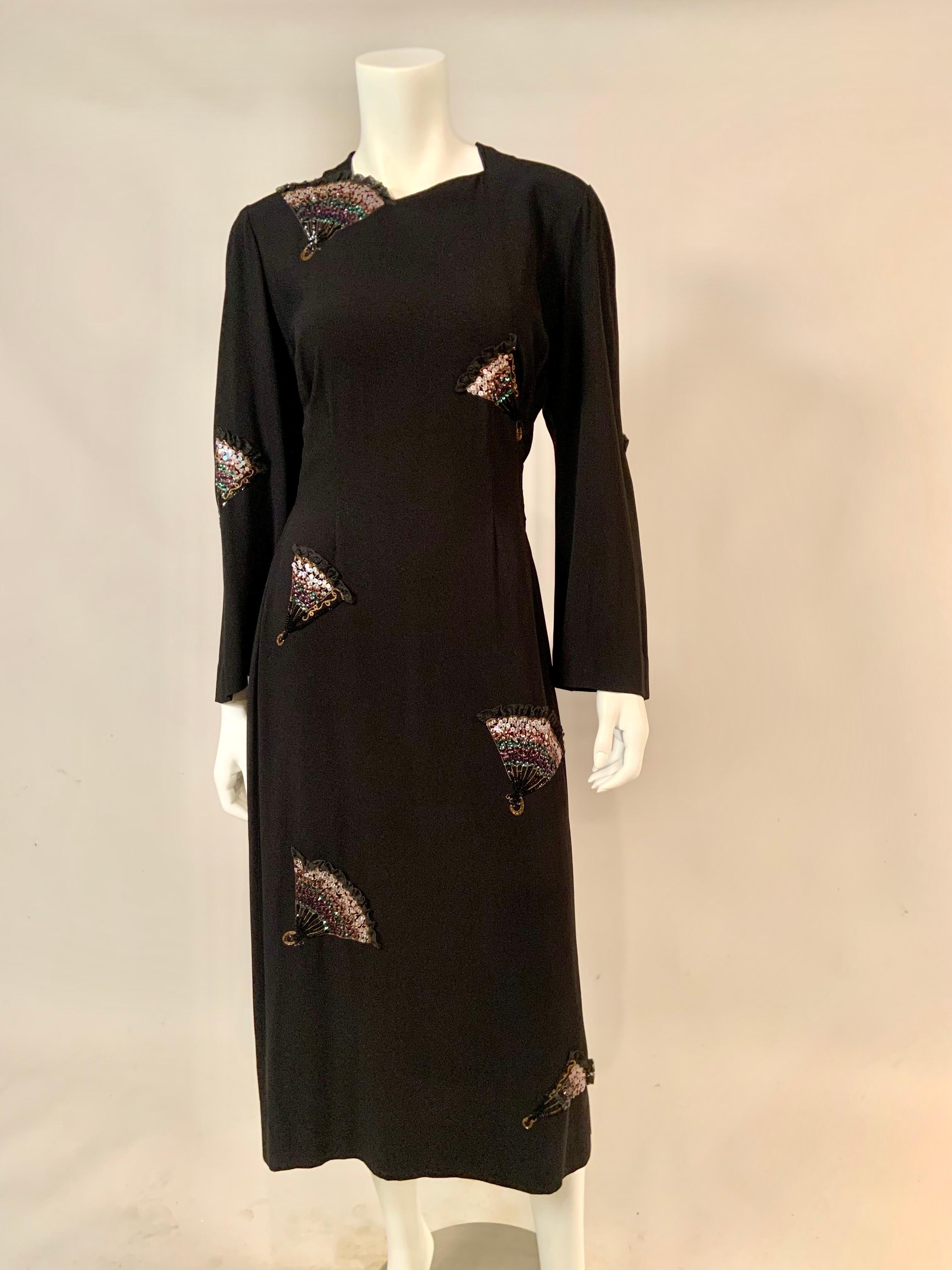 This 1940's black crepe evening or cocktail dress has a striking design of embroidered, beaded and lace trimmed fans on the front and back of the dress.  Some fans are fully open and some are partially closed.  They all have gold metallic thread