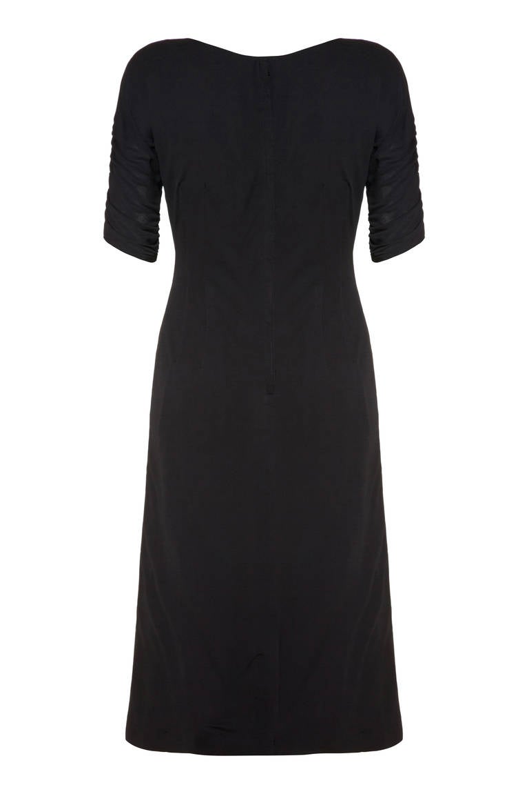 This 1940s black wiggle dress is a fantastic example of early rayon jersey.  It is of superb quality and is likely a high-end American made department store piece. It features ¾ length ruched sleeves and an unusual intertwined rope and tassel detail