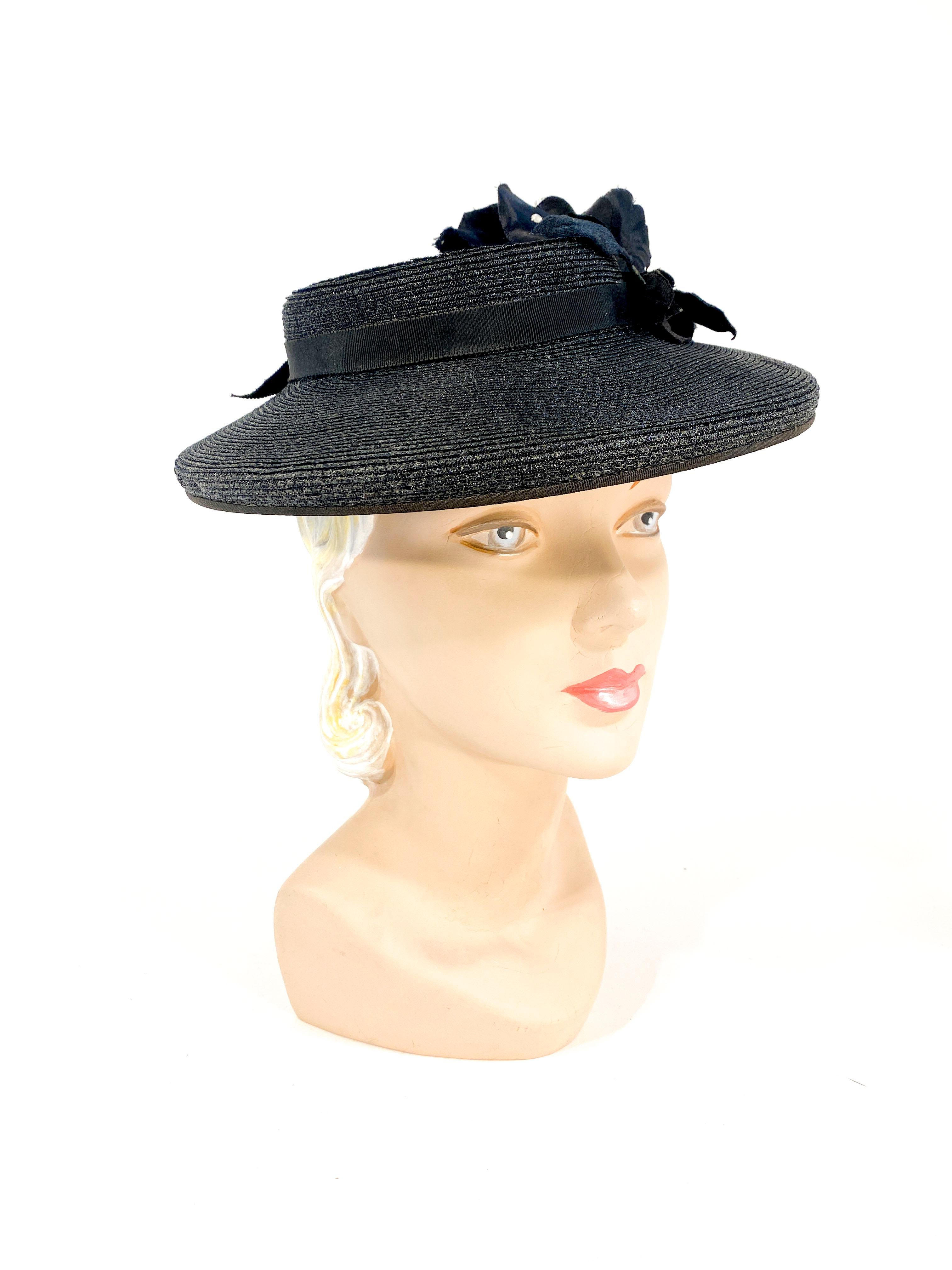 1940s black coated and woven straw hat with a shallow sculpted crown decorated with a thin grosgrain band/bow, and a large handmade silk flower touched with clear rhinestones. The brim is structured with a mild curve. 