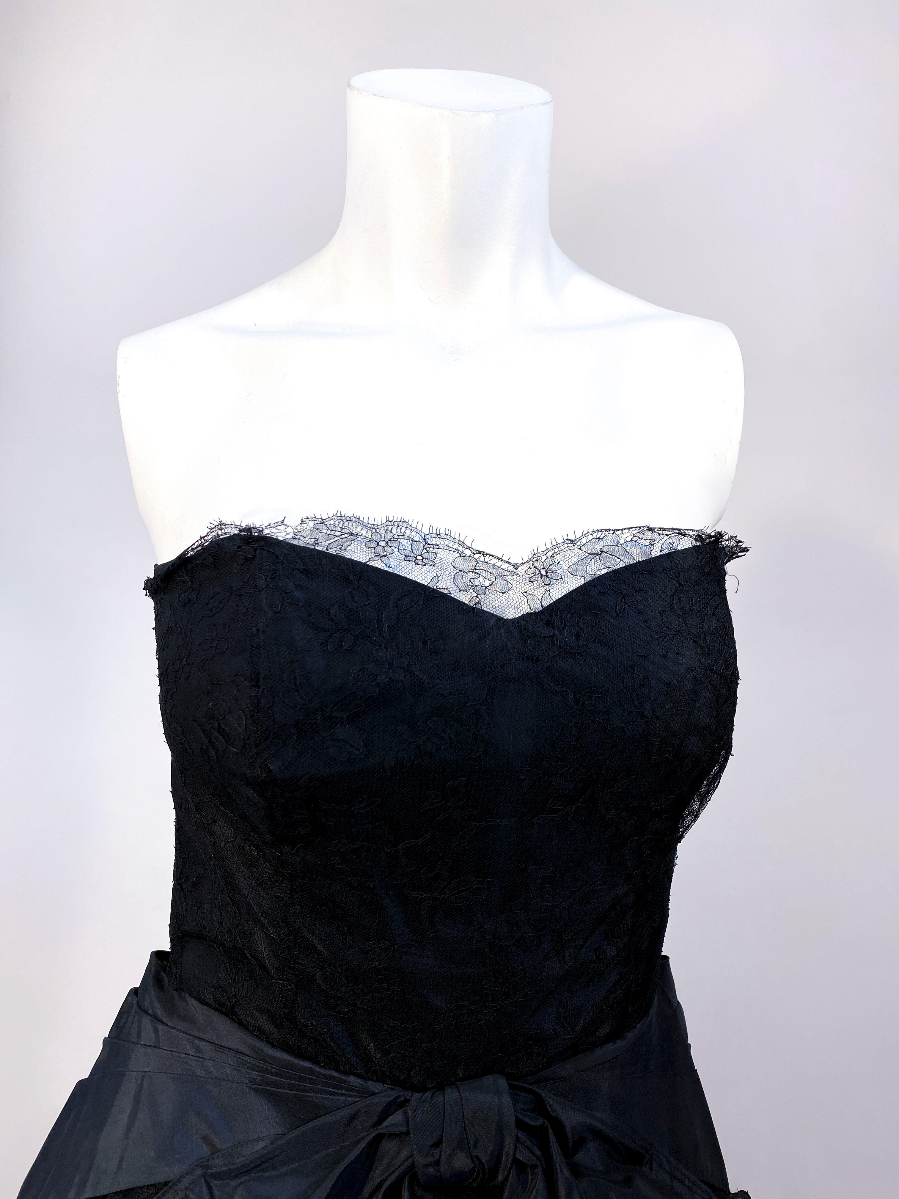 Late 1940s black full-length taffeta ball gown with Chantilly lace trim along the strapless bodice, an enlarged bow, a faux bustle in the back that is pleated and goes down three-fourths of the way down the skirt, metal side zip closure, and banning