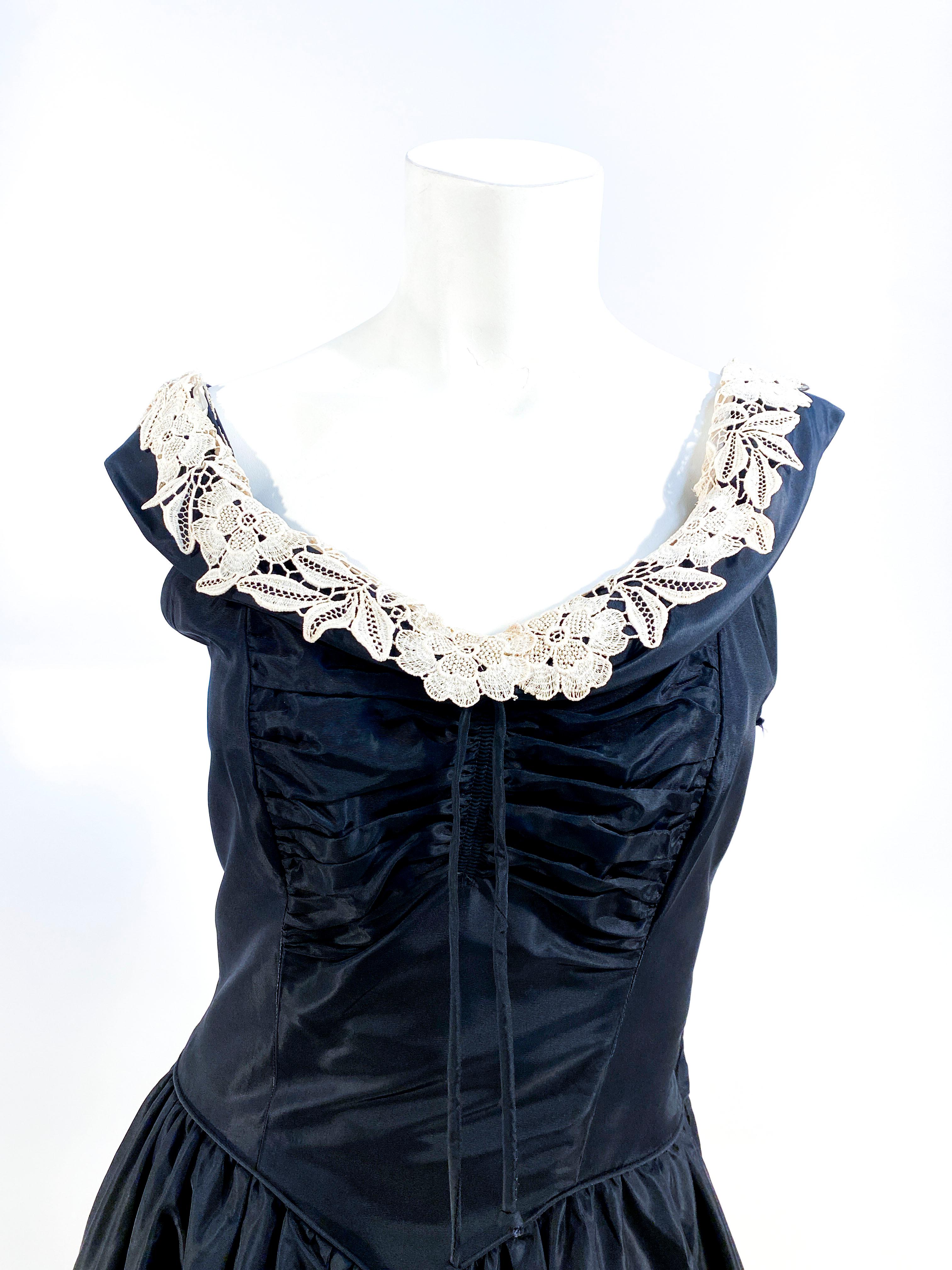 Early 1940s custom made black taffeta evening gown with a fitted, ruched, and tied bust. The boat neckline is rounded with a lace accent rolled over the collar. The bodice is sleeveless and the side has a metal zipper. The piped waist band has