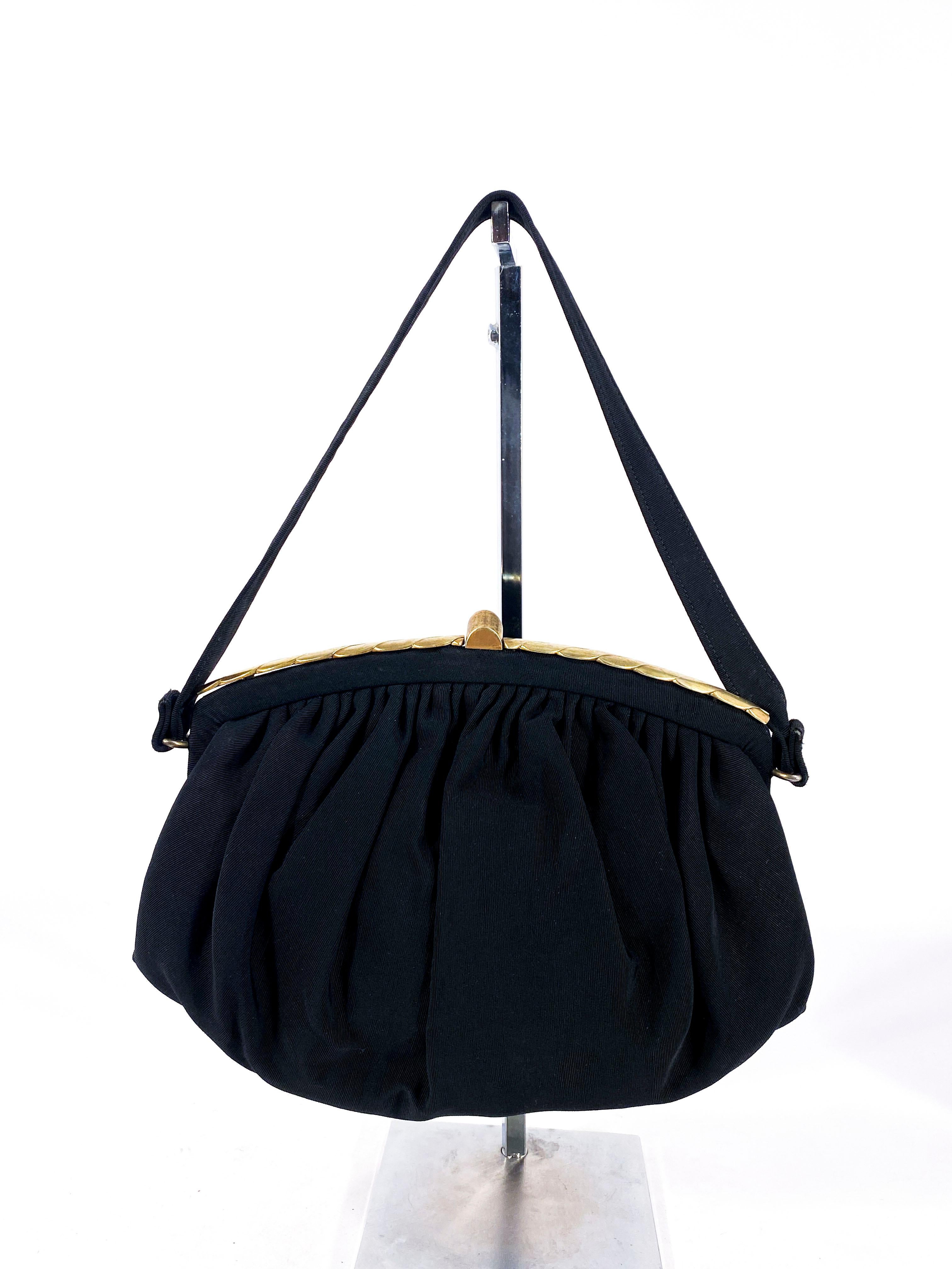 1940s Black twill purse with a decorative brass closure, gathered body toped with decorative frame. The interior of the purse is made of a black lining with several pocket and one of them with a zip closure. 