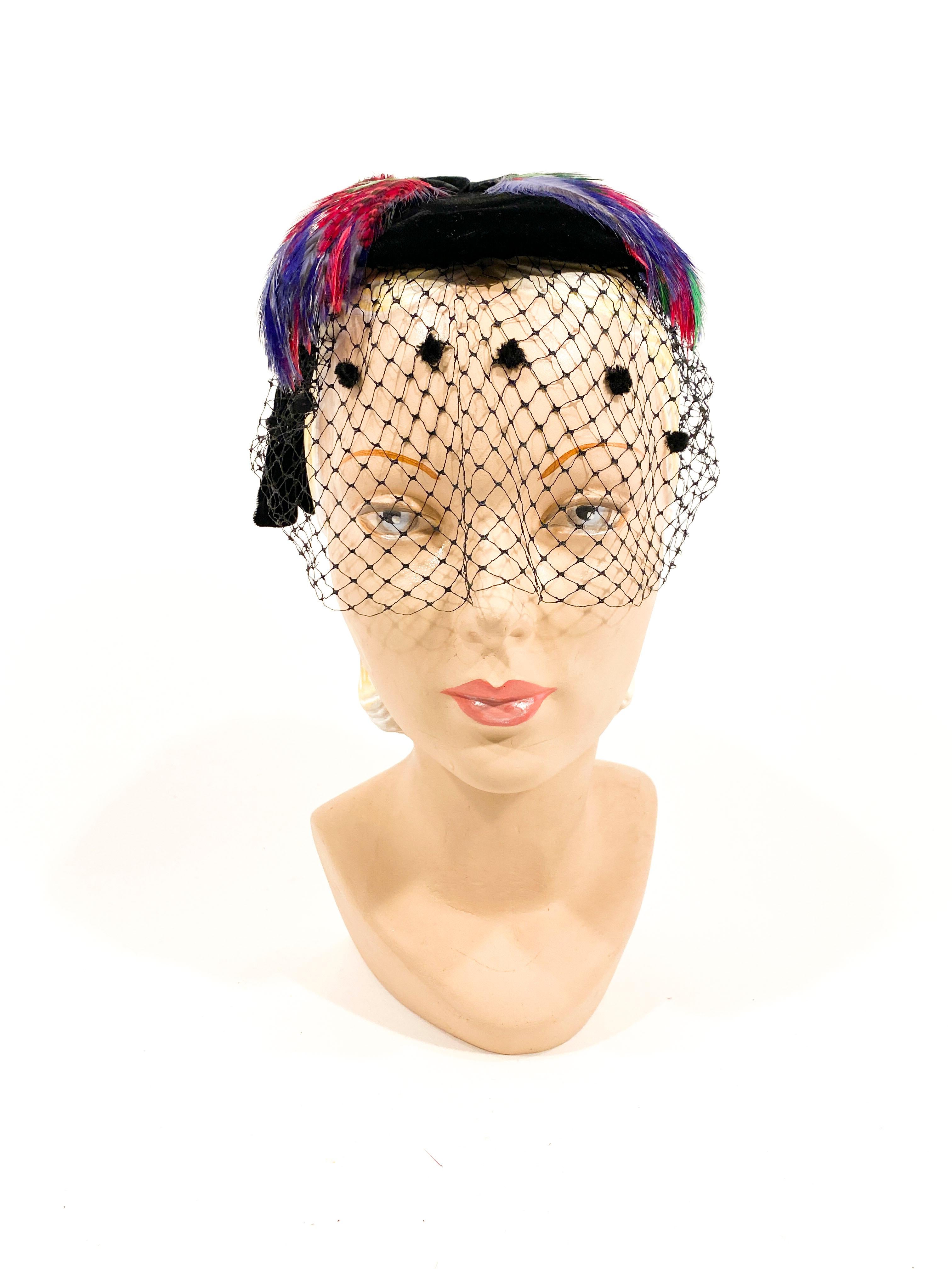 194s black silk velvet cocktail hat with handmade decorative loops adorning the back of the head. The top is decorated with multi-colored feathers and front has a veil accented with small velvet tuffs. The interior has a comb to secure the hat to