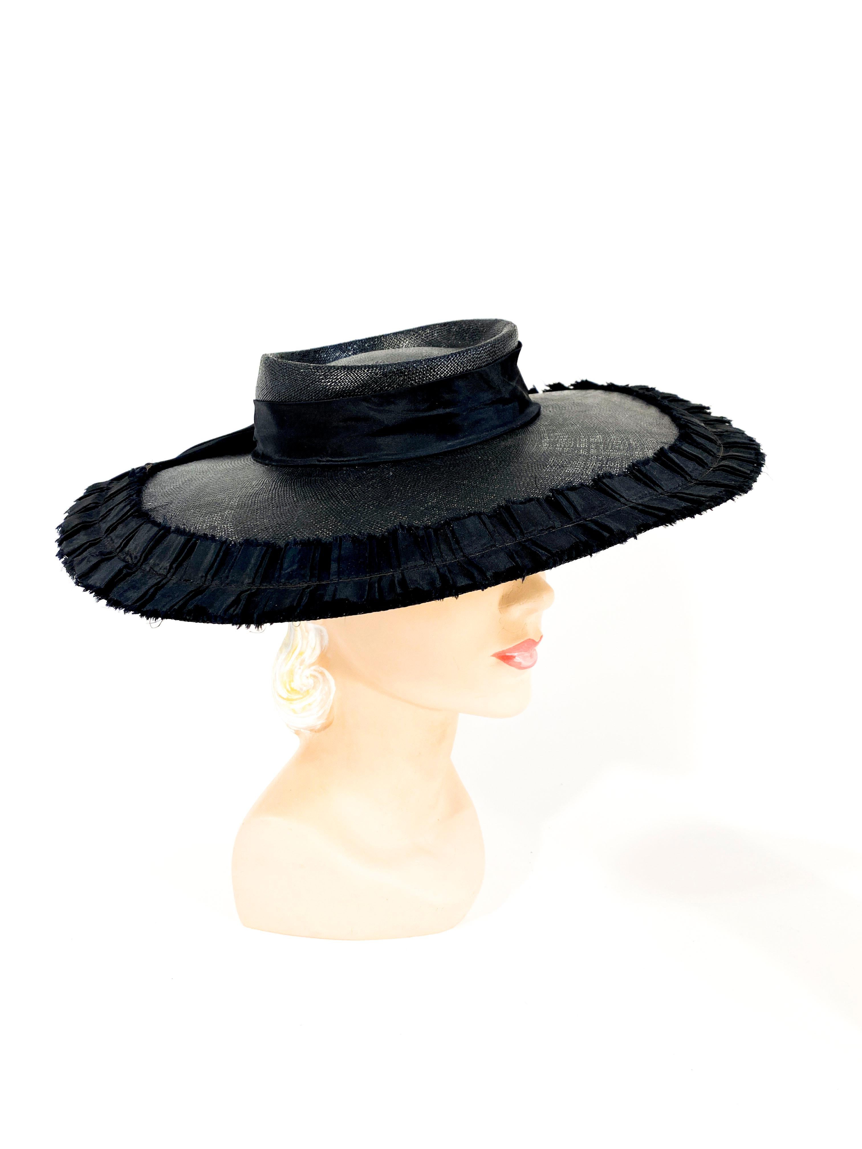 1940s black coated woven straw hat with a wide brim boarded with a black taffeta pleated trim. The shallow crown has a decorative black twill band. The wide grosgrain security band is attached to the interior of the hat and worn on the back of the