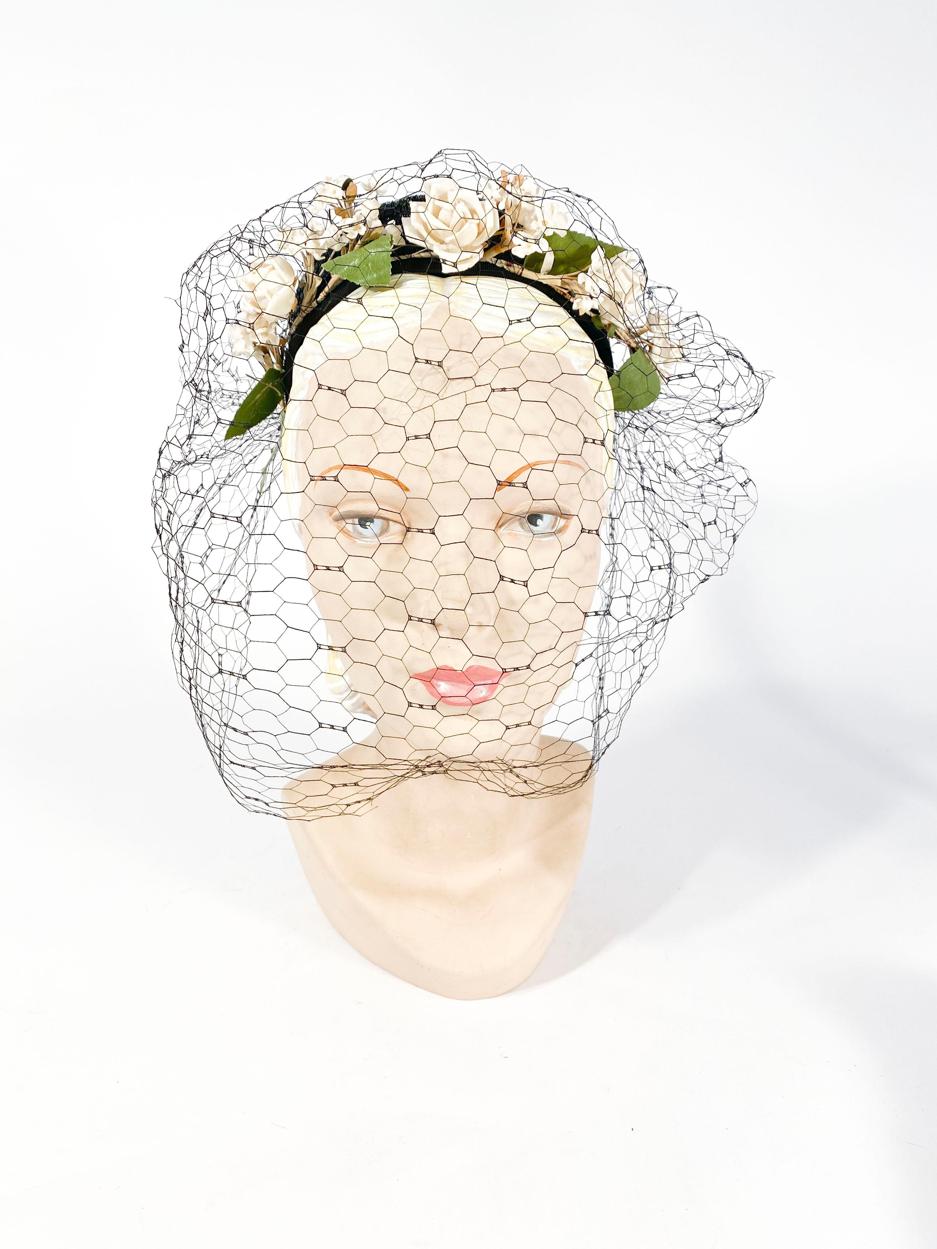 1940s black coated and woven straw hat with a wreath of off-white flowers garnished with green leaves and a full face veil 