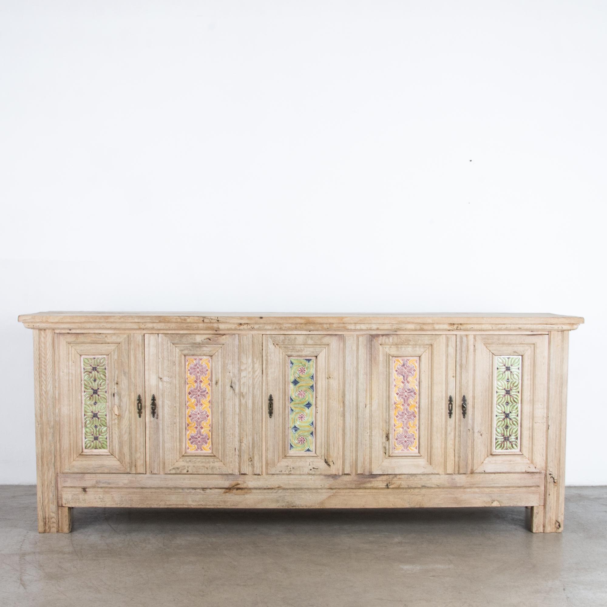 A bleached oak buffet from Belgium, circa 1940. Two pairs of double doors and one single door open onto an interior shelf. Glazed tiles in bright, symmetrical patterns decorate the door panels. The restored wood is light and natural, while the