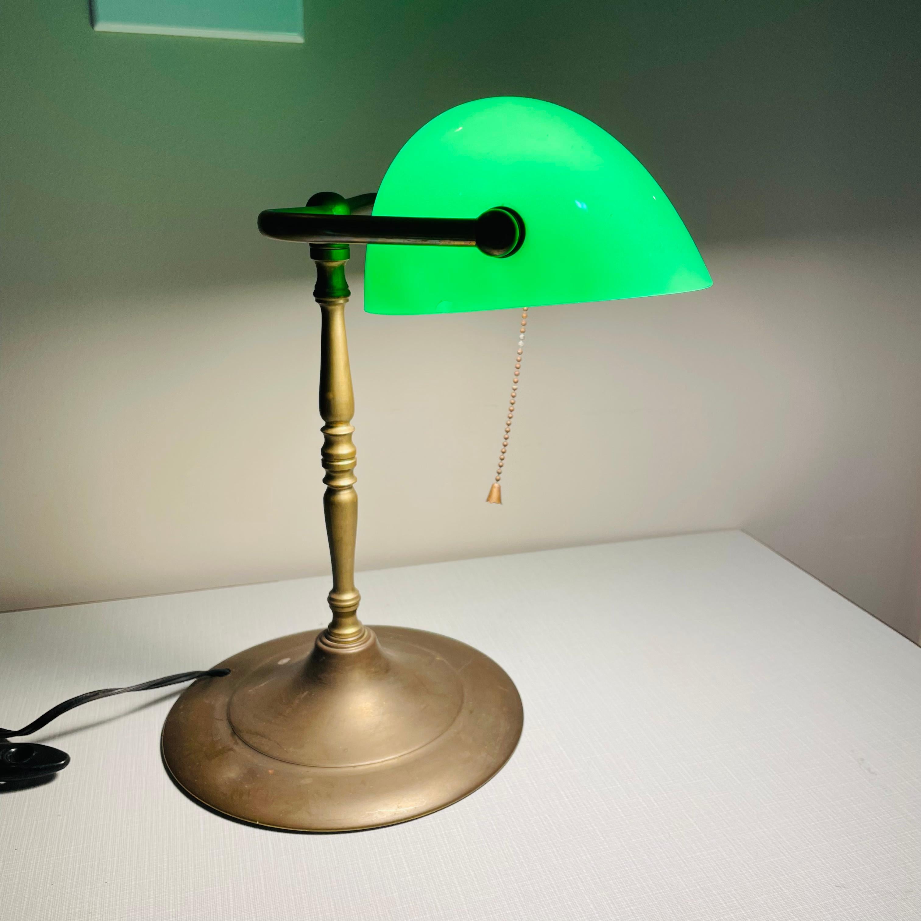Vintage Art Deco Banker lamp with a green glass shade and brass base and arm. The lamp has newer wiring, and uses a standard light bulb. Perfect for a hall table or one's desk. Classic and timeless style. The shade articulates to adjust the amount