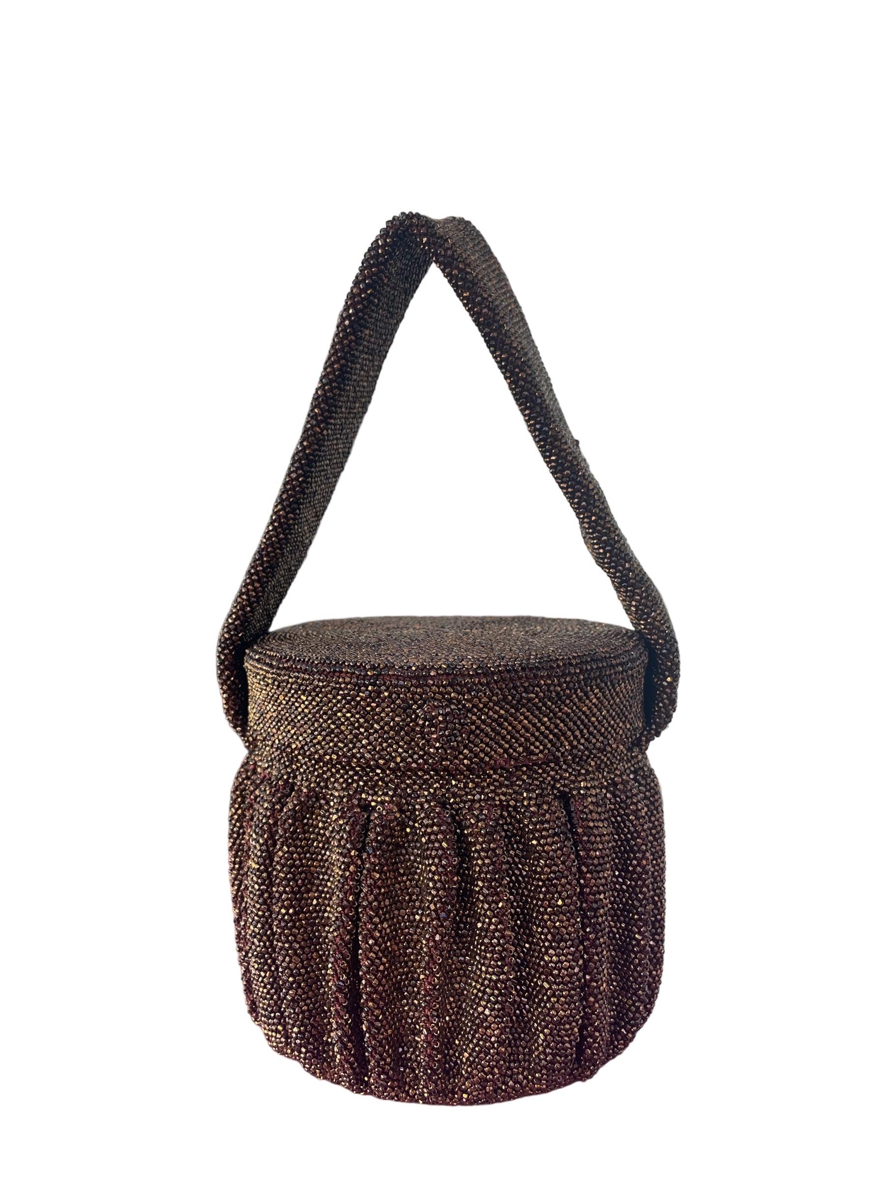 1940s Bronze Steel Cut Bead Circular Box Bag w/ Mirror

Sac seau de forme circulaire avec extérieur en perles de verre bronze et détails plissés.

Couvercle attaché avec miroir circulaire à l'intérieur. Intérieur en satin marron. Quelques taches
