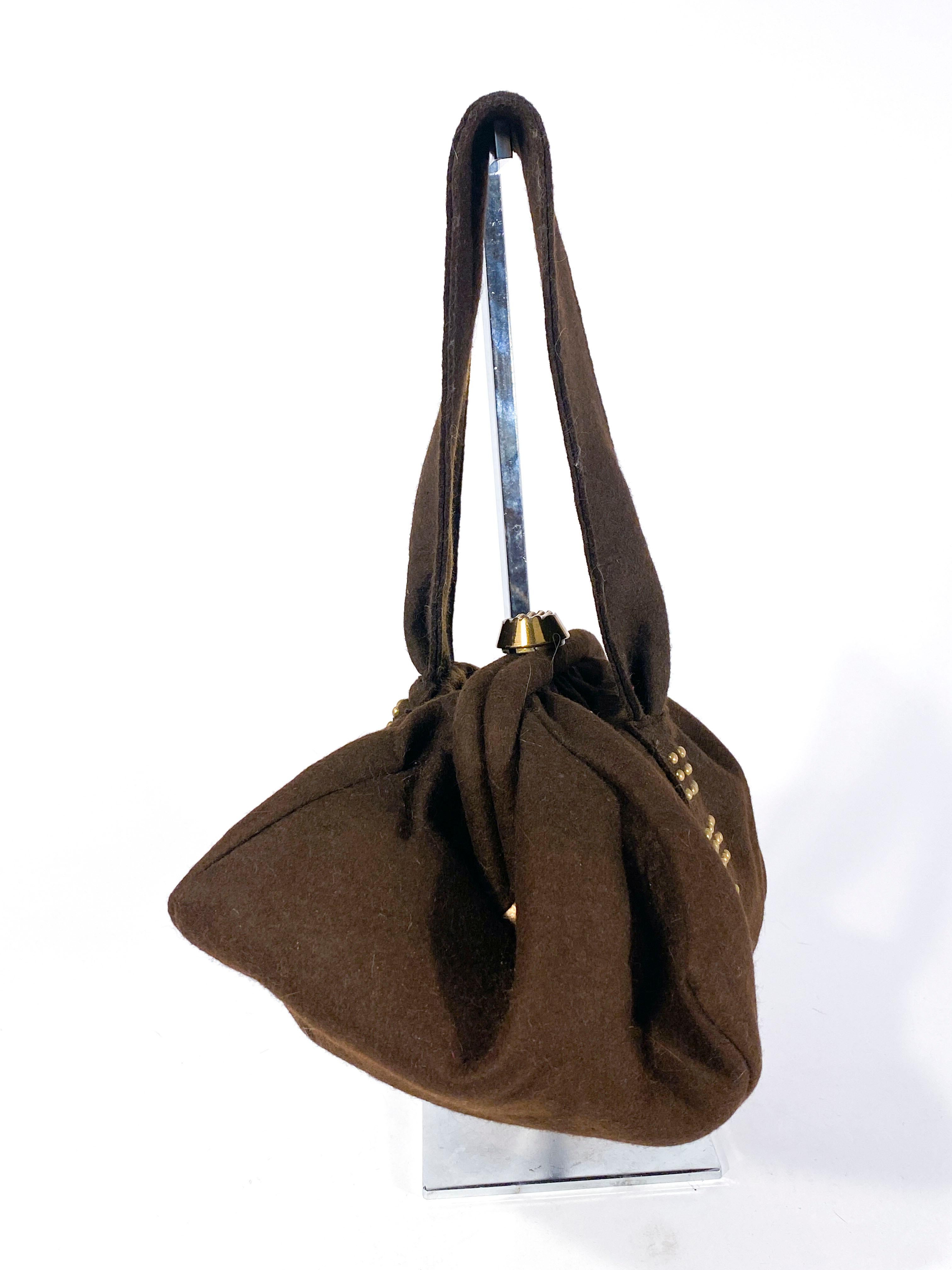 1940s brown fur felt daytime handbag gathered at the structured flip-back closure. The body of the bag is decorated with brass rounded studs and finished with an extra wide wrist strap. The interior is lined with on interior pocket. 