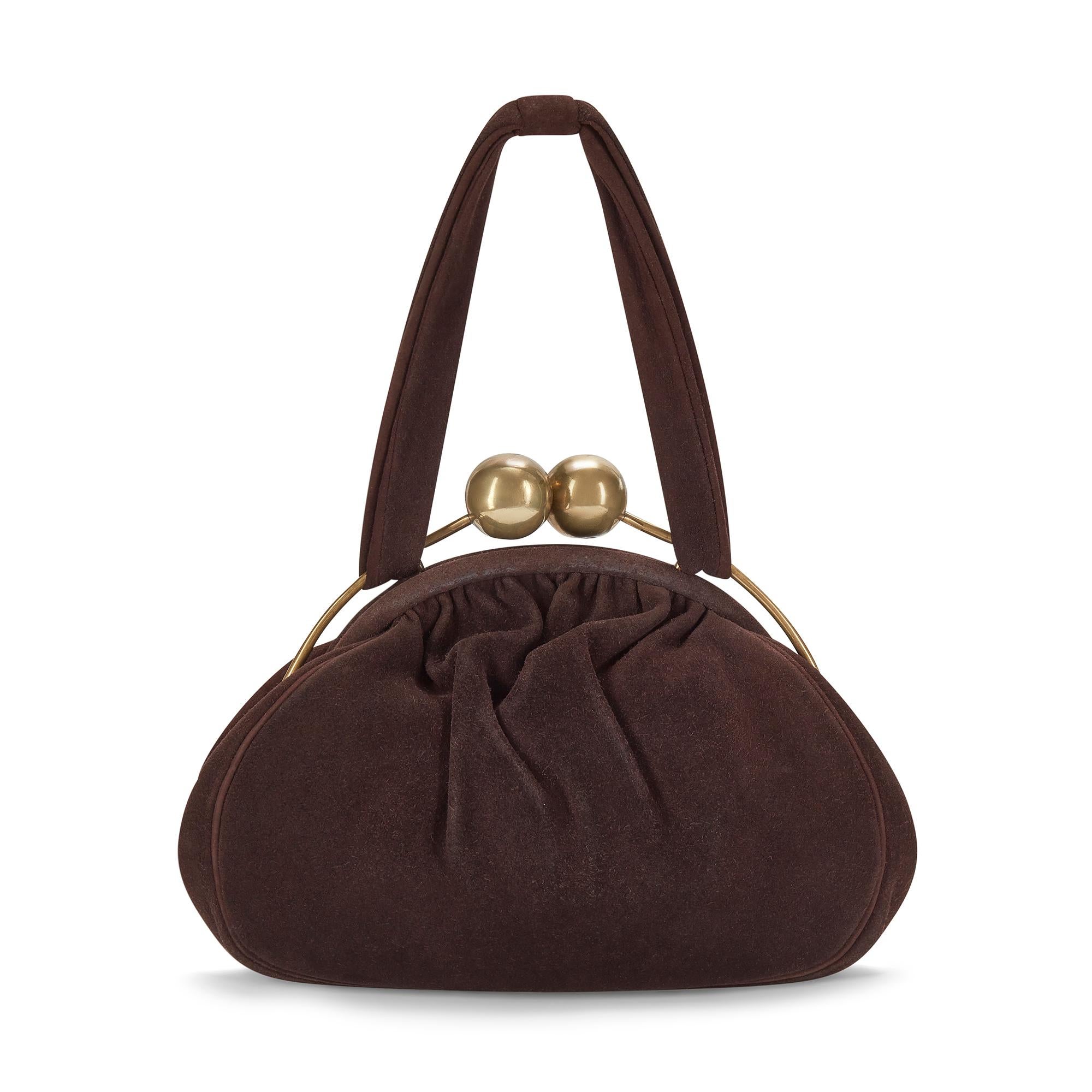 This unusual late 1940s bag is crafted from luxurious, rich brown suede in a pouch-like shape. The brass hardware is exposed at the top of the bag and fastens with two chunky oversized spheres that form a clasp. This tactile bag is lined with