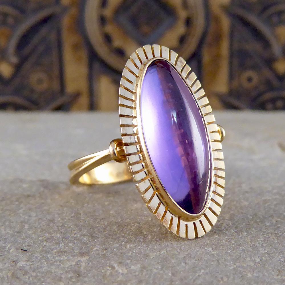 This ring features one single smooth Cabochon Amethyst in a collar set mould holding it in place. Surrounding this enchanting stone is a detailed cut-in effect halo rim crafted in 14ct Gold, along with the 14ct Gold band with a European Hallmark on