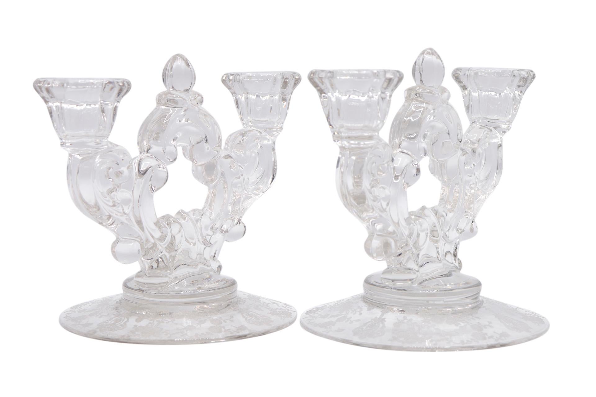 Une paire de candélabres en verre gravé des années 1940 fabriqués par Cambridge Glass. Deux chapiteaux anglés sont soutenus par des tiges à volutes qui se rejoignent au centre par un épi de faîtage en forme de gland. La base est gravée du motif