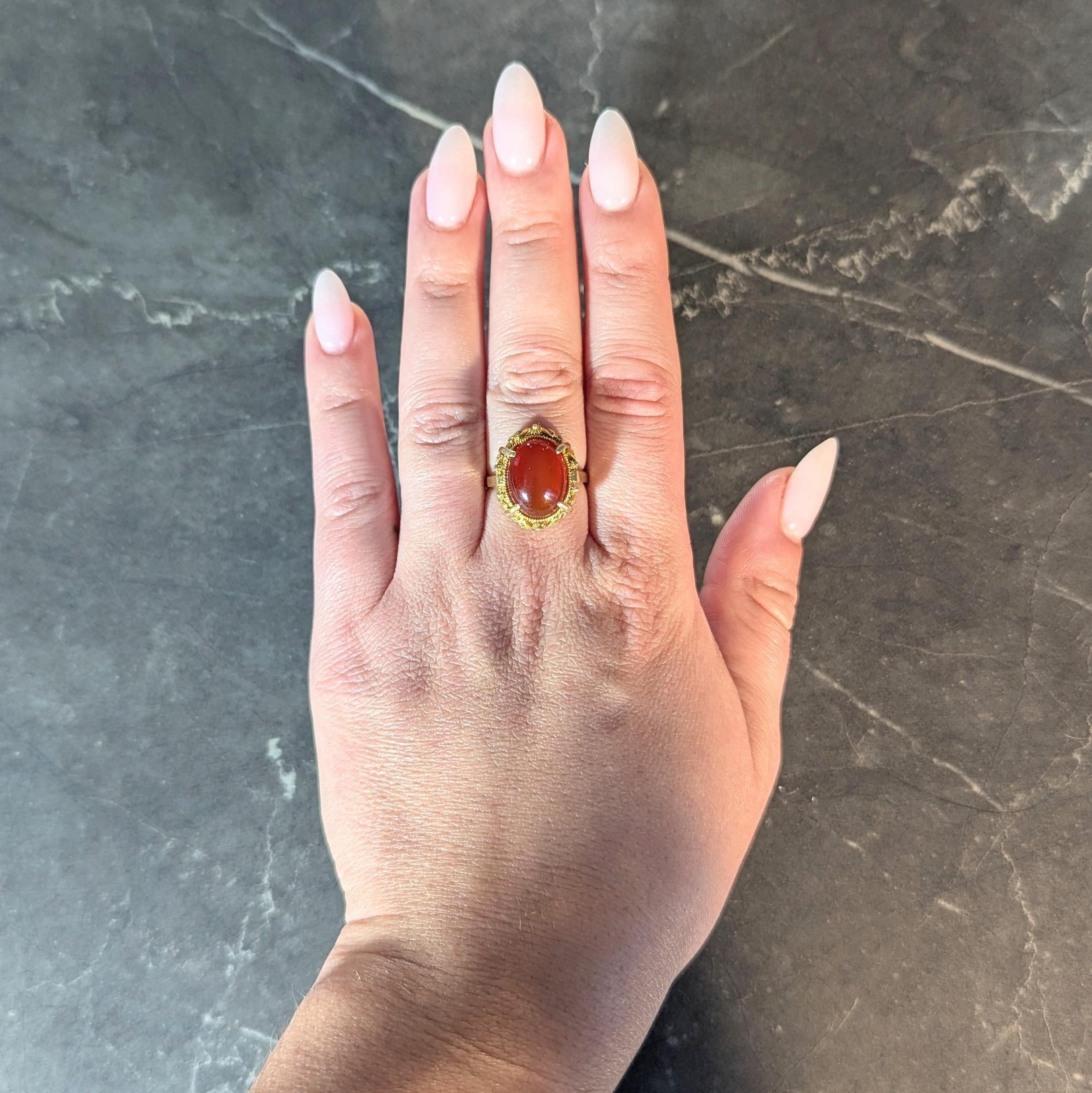 Centering an oval shaped carnelian cabochon measuring 10.5 x 15.0 mm
Translucent reddish orange in color - prong set with twisted rope bezel
Featuring a domed filigree mesh surround with floral appliqué
Accented by gold granulation