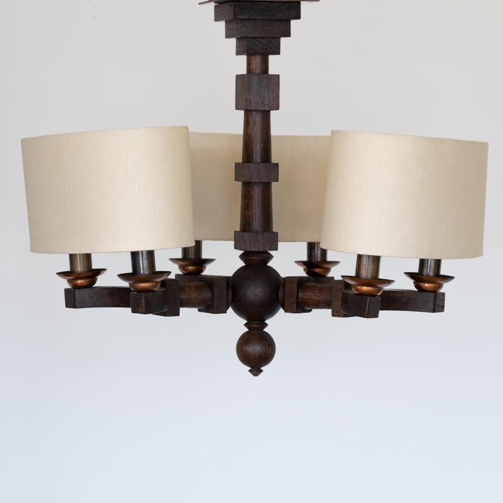 Unique carved wood chandelier by Charles Dudouyt from France, 1940s. Flush mount chandelier with three arms and six sockets. Geometric carved wood frame and brass bobeche detail. Newly rewired with three new oval linen shades. Original finish shows