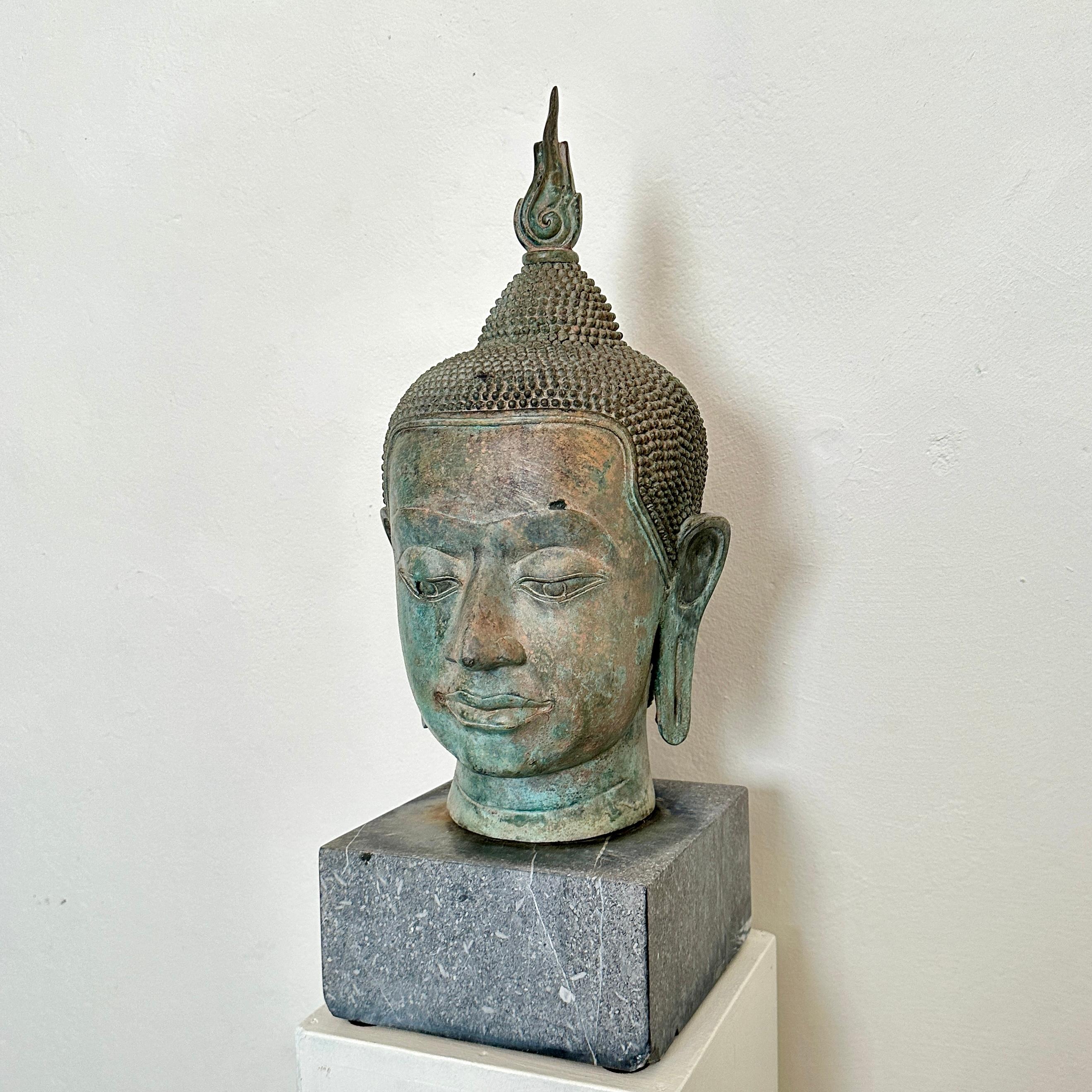 Dieser Sukhothai-Buddha-Kopf aus Bronzeguss der 1940er Jahre strahlt Ruhe und zeitlose Schönheit aus und ruht gelassen auf einem Sockel aus grauem Granit. Durch die Verschmelzung von künstlerischer Meisterschaft und spiritueller Bedeutung fängt die