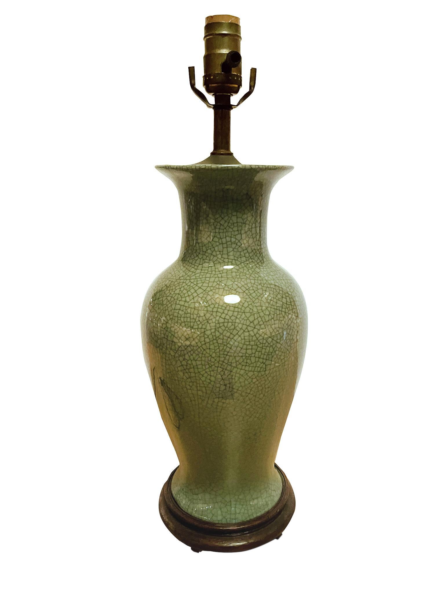 This elegant ceramic lamp was made in the 1940s. It has a wonderful crackle glaze in a celadon green hue. It is newly rewired and paired with a custom-fitted pleated silk shade. The lamp's base is a wood and its top hardware is