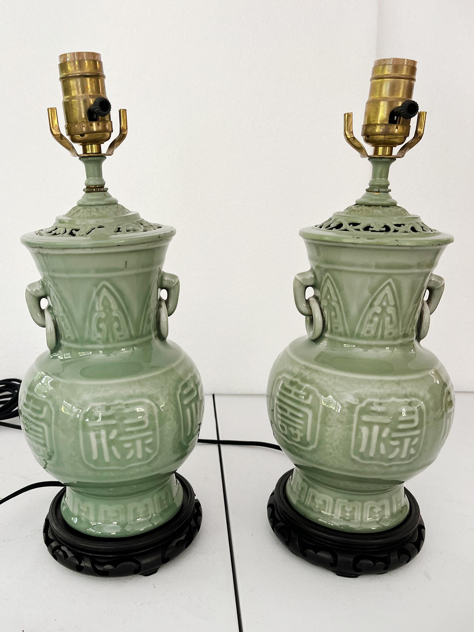 Crafted in the 1940s, these table lamps have ceramic bodies, brass hardware, and ebonized wood bases. The ceramic bodies are in an elegant urn form and have an exquisite celadon green glaze. The lamps have been newly rewired with single bulb sockets