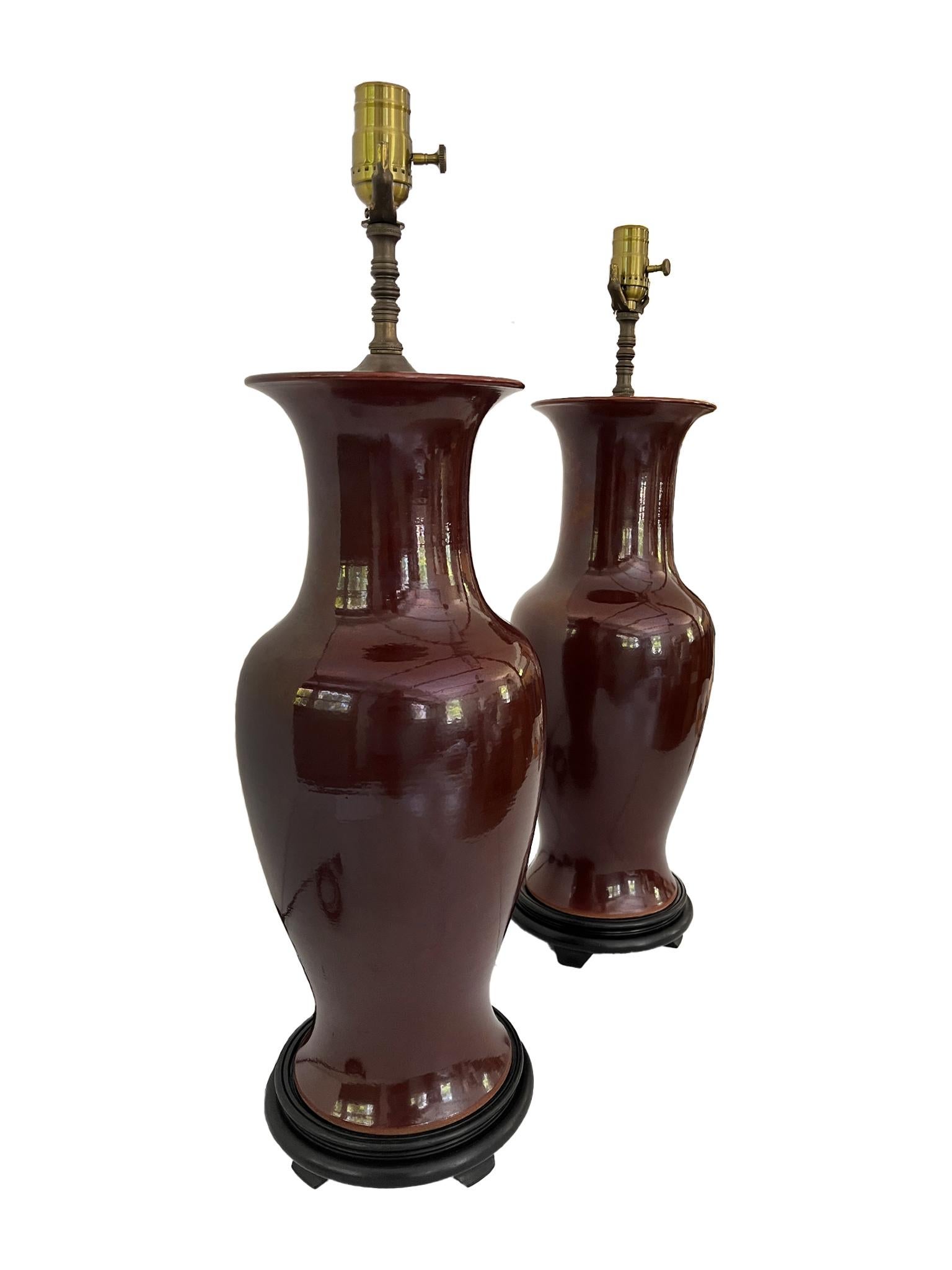 Paire d'élégantes lampes de table composées de vases en céramique chinoise, de ferrures en laiton et de bases en bois ébonisé. La céramique a une riche glaçure sang-de-bœuf. Le câblage des lampes a été refait  et remis à neuf avec de nouvelles
