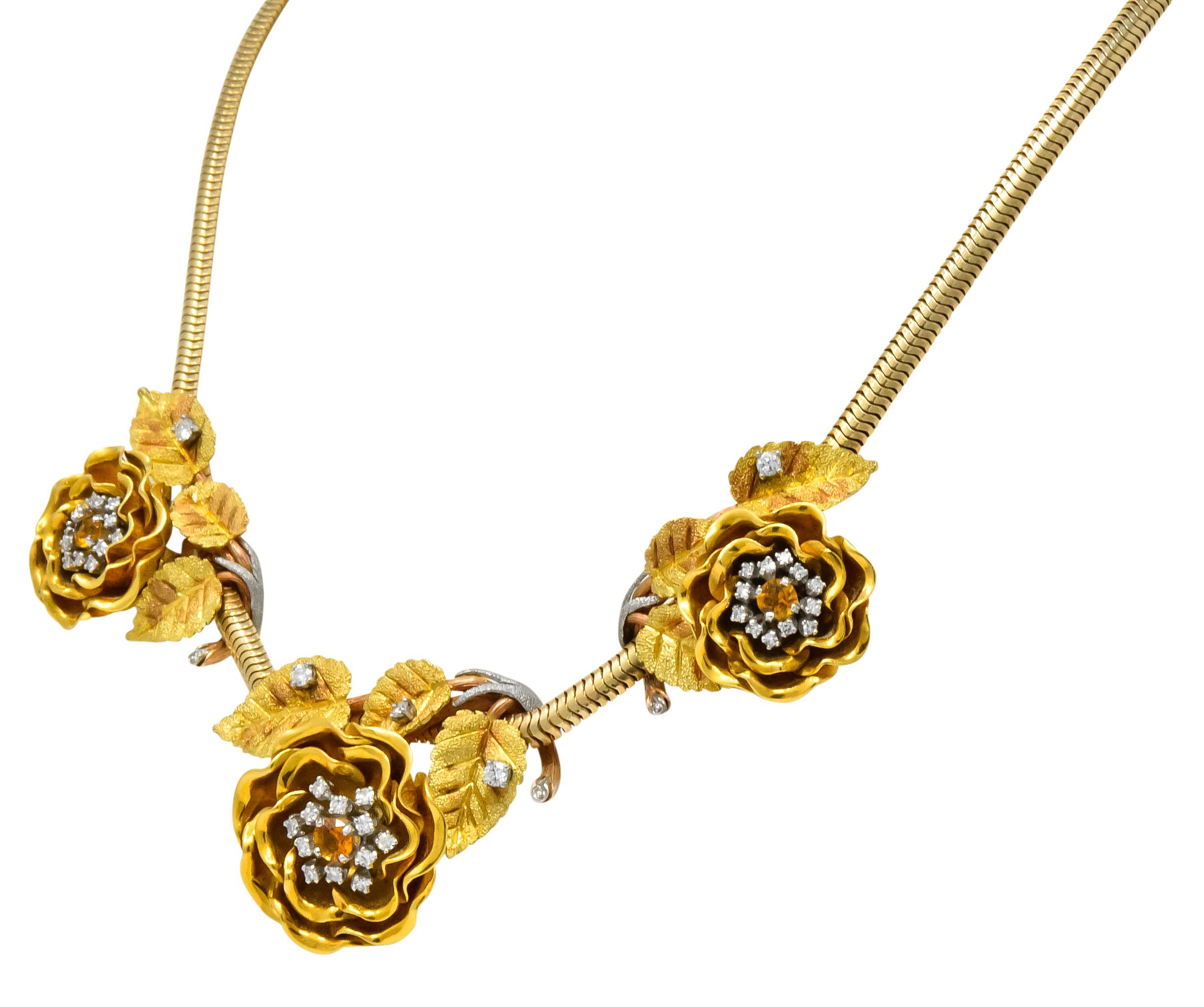 Centering three highly rendered gold flowers surrounded by green gold foliage terminating in rose and white gold stems

Each centering a round cut citrine weighing in total 0.55 carat; transparent and bright yellowish-orange in color

Accented