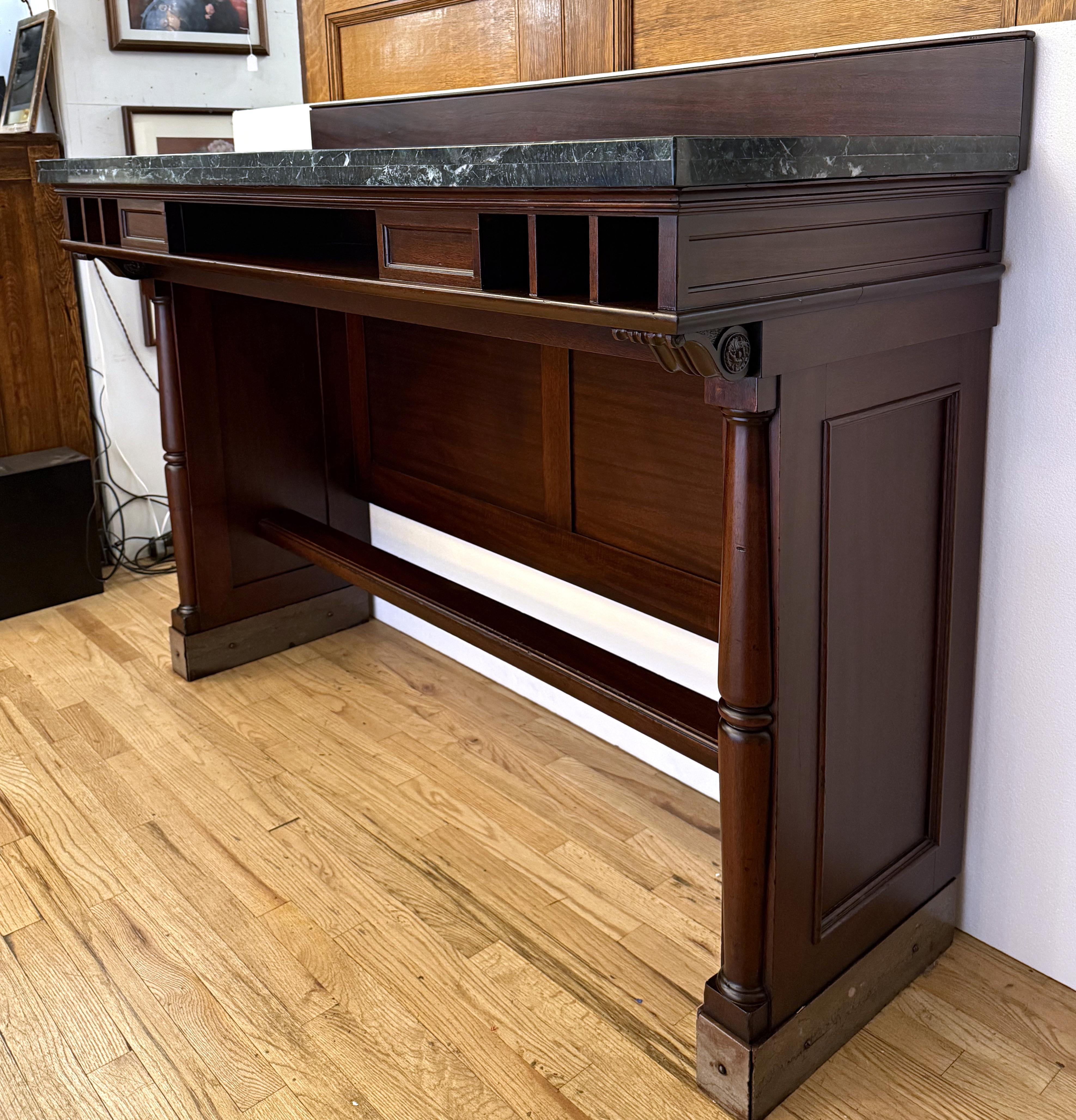 Mesa de banco de una cara de los años 40 con madera teñida de oscuro, tapa de mármol veteado verde y placas de latón en la base. Presenta siete compartimentos en la parte delantera. Esta pieza ha sido restaurada recientemente. Uno disponible. Ten en