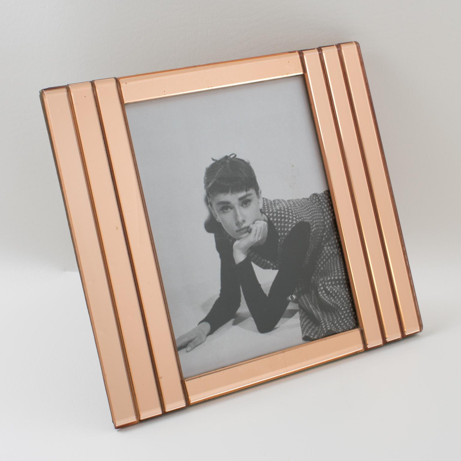 Elegant 1940s French Hollywood Regency mirrored picture photo frame. Deep beveling and three-flat sticks of mirrored glass on sides in lovely copper or pink-peach color. The frame can only be placed in a portrait position. Back and easel in cognac