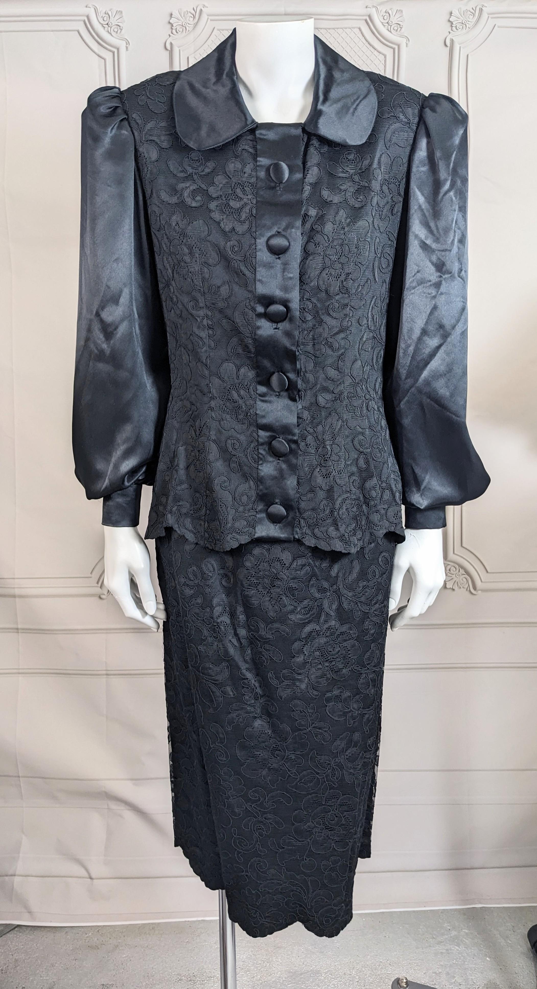 Charming Cotton Lace and Silk Satin Cocktail Suit from the 1940's. Strong shouldered, fitted suit in silk satin with full gathered sleeves. Both bodice and skirt are overlaid in cotton lace with satin placket, buttons and Peter pan collar. Scalloped