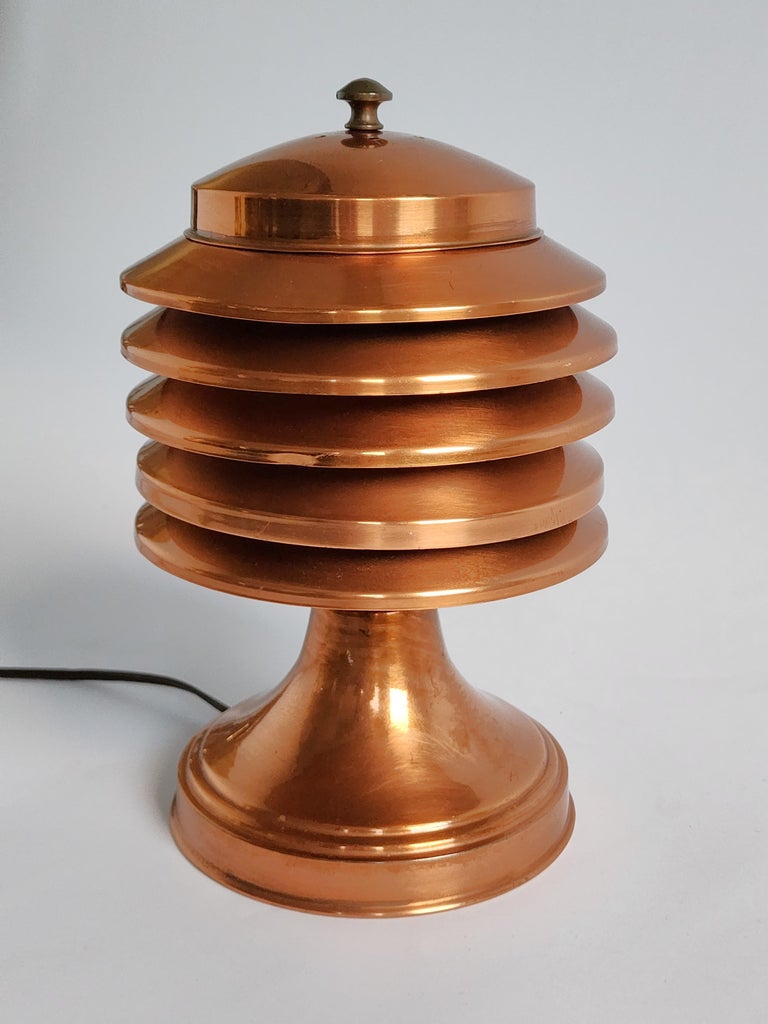Iconique lampe de table en cuivre à cinq niveaux, de style Art Déco et de l'ère de la machine, de marque Coulter.

Le couvercle ventilé permet d'accéder à l'ampoule.

Interrupteur rotatif marche/arrêt sur le côté.

Contient une douille de