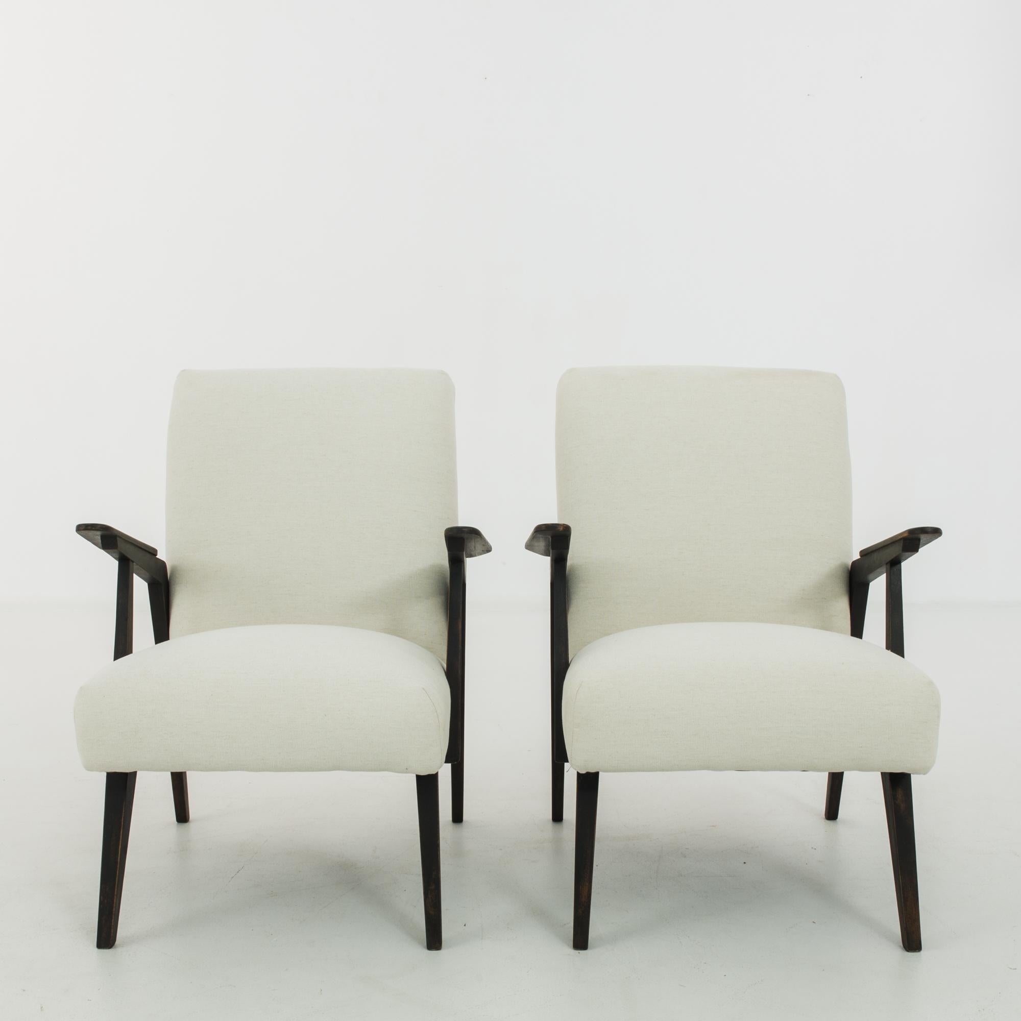 This pair of upholstered wooden armchairs was made in Czechoslovakia, circa 1950. Upturned angular armrests and tapered, splayed legs give the chairs a sense of motion, underscored by geometric seat cushions. The newly upholstered seats and backs