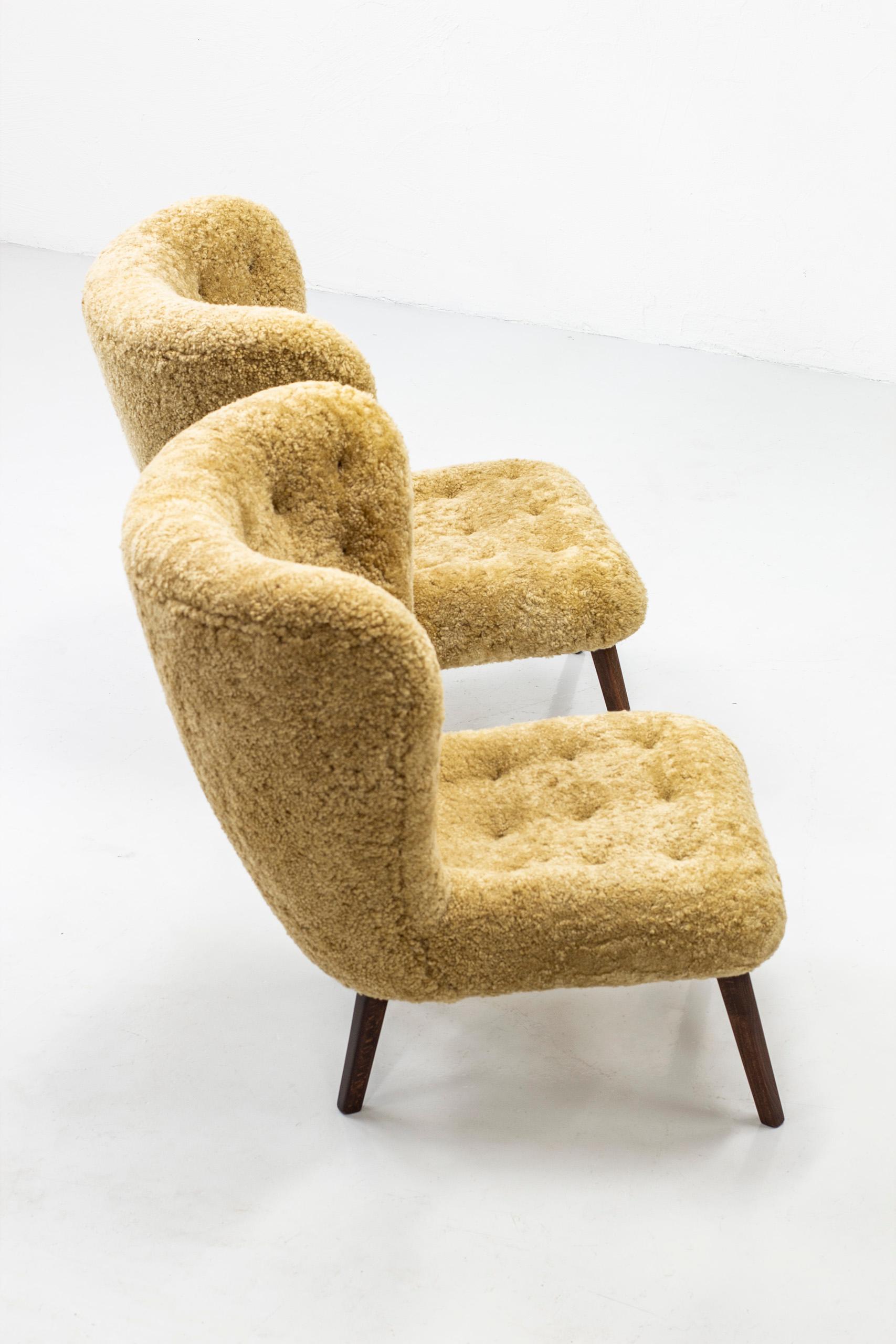 Pair of exquisite lounge chairs in the manner of Viggo Boesen. Produced in Denmark during the 1940-50s. Rare aesthetic with a large oversized back rest. Tufted with about 40 buttons on each chair. Restored dark stained oak legs and new sheep skin