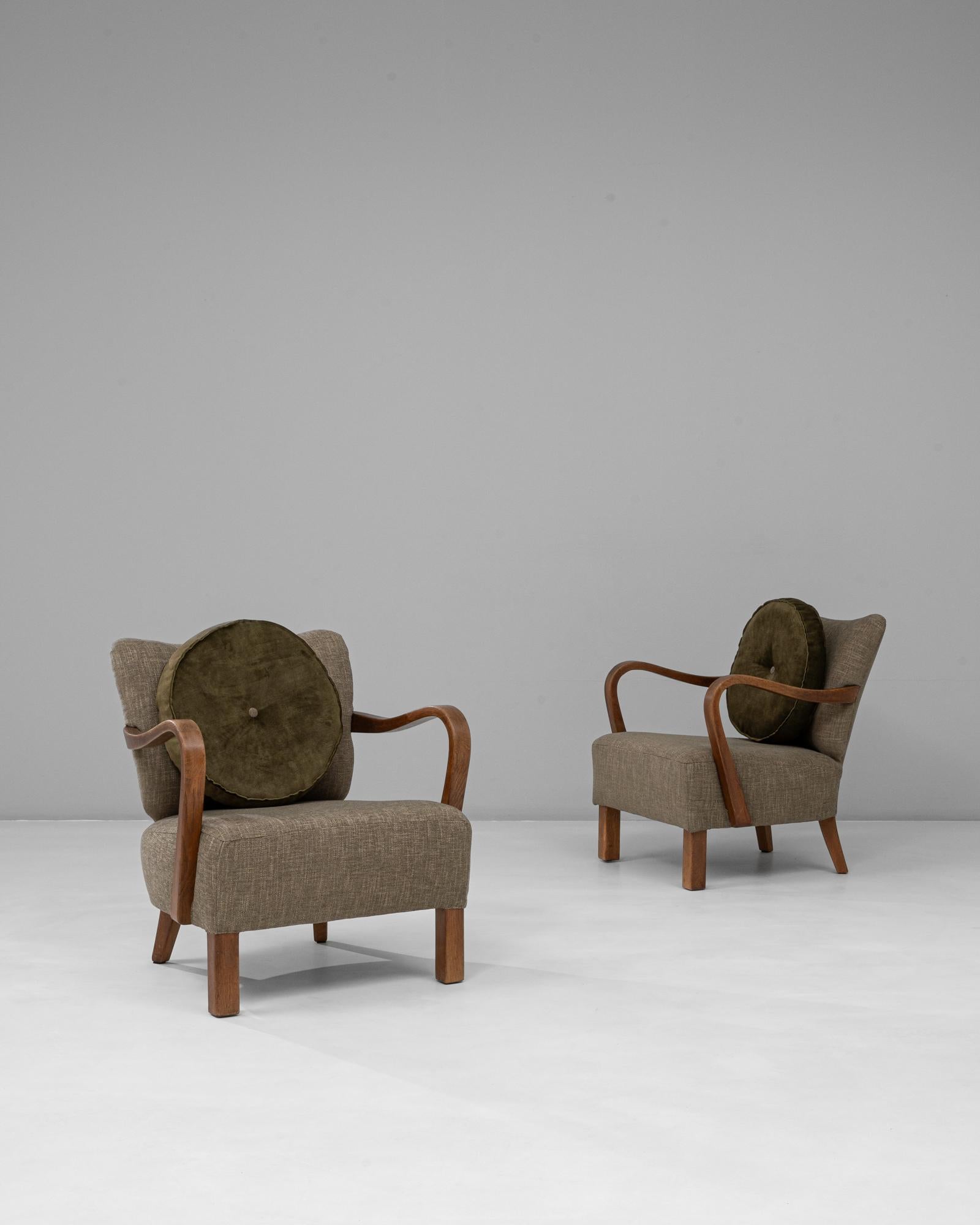 This 1940s Danish pair of Art Deco upholstered armchairs exemplifies mid-century craftsmanship with a distinctly Scandinavian sensibility. Each chair features sculptural bentwood arms, subtly flared legs, and a generously cushioned seat and back,