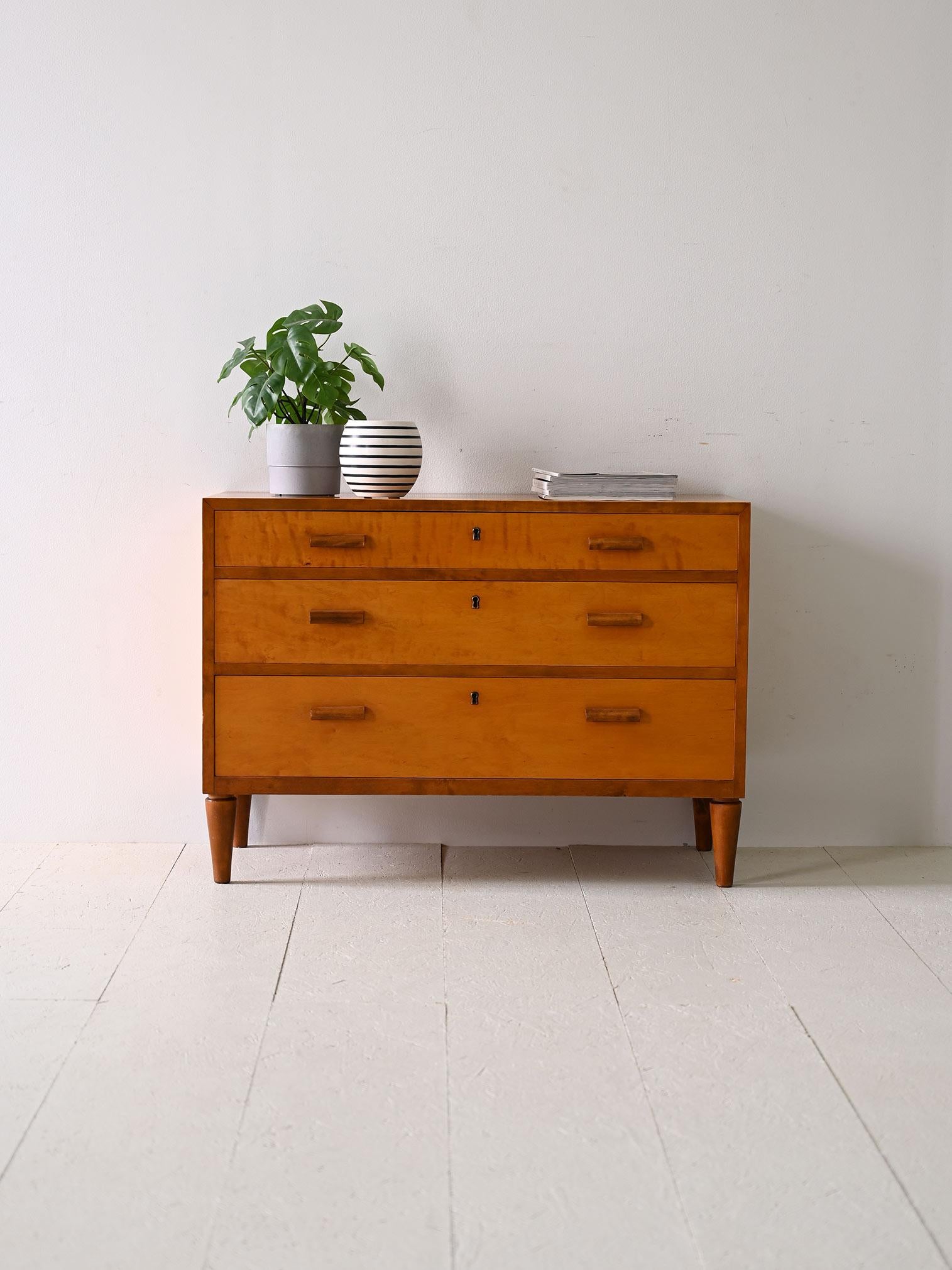 Scandinavian Deco chest of drawers produced in the 1940s.

The square shape and rectangular carved wooden handles lend a unique character to this original vintage piece of furniture.

All three drawers are lockable.

Good condition. A conservative