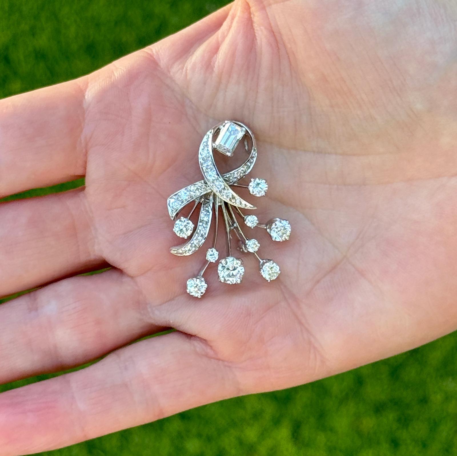 This exquisite piece from the 1940s is a versatile and captivating example of vintage jewelry design, crafted in radiant 14 karat white gold. The brooch, designed in a graceful spray motif, features an array of sparkling old European cut and emerld