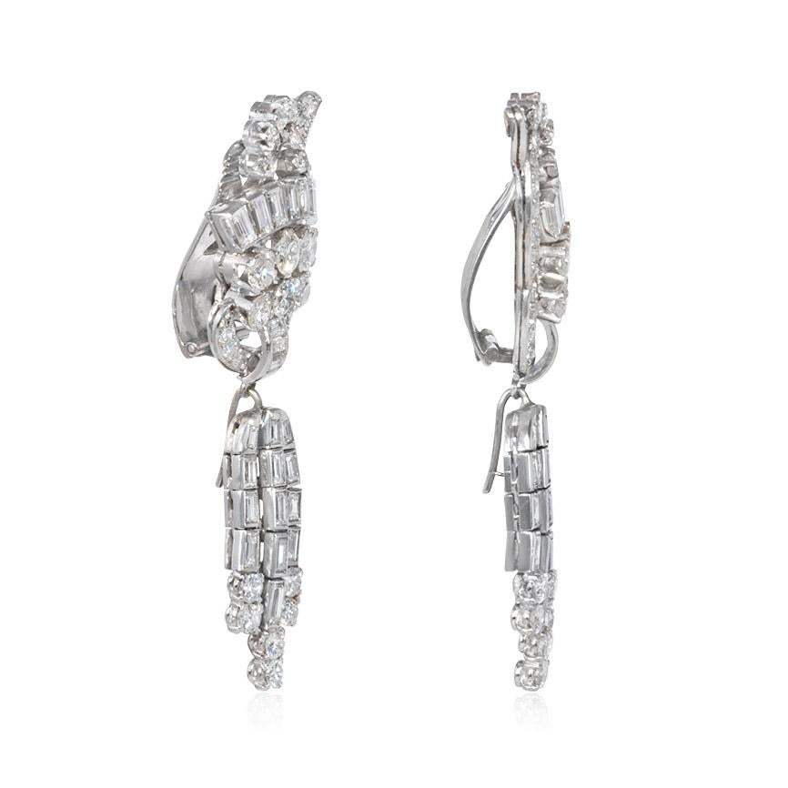 A pair of Retro day-to-night diamond earrings with scrolled tops and detachable tassel pendants, in platinum.  Atw 6.50 ct. round, baguette and single cut diamonds.  5.5 cm long, tops alone 3 cm

Custom-designed pendants - with pearls or colored