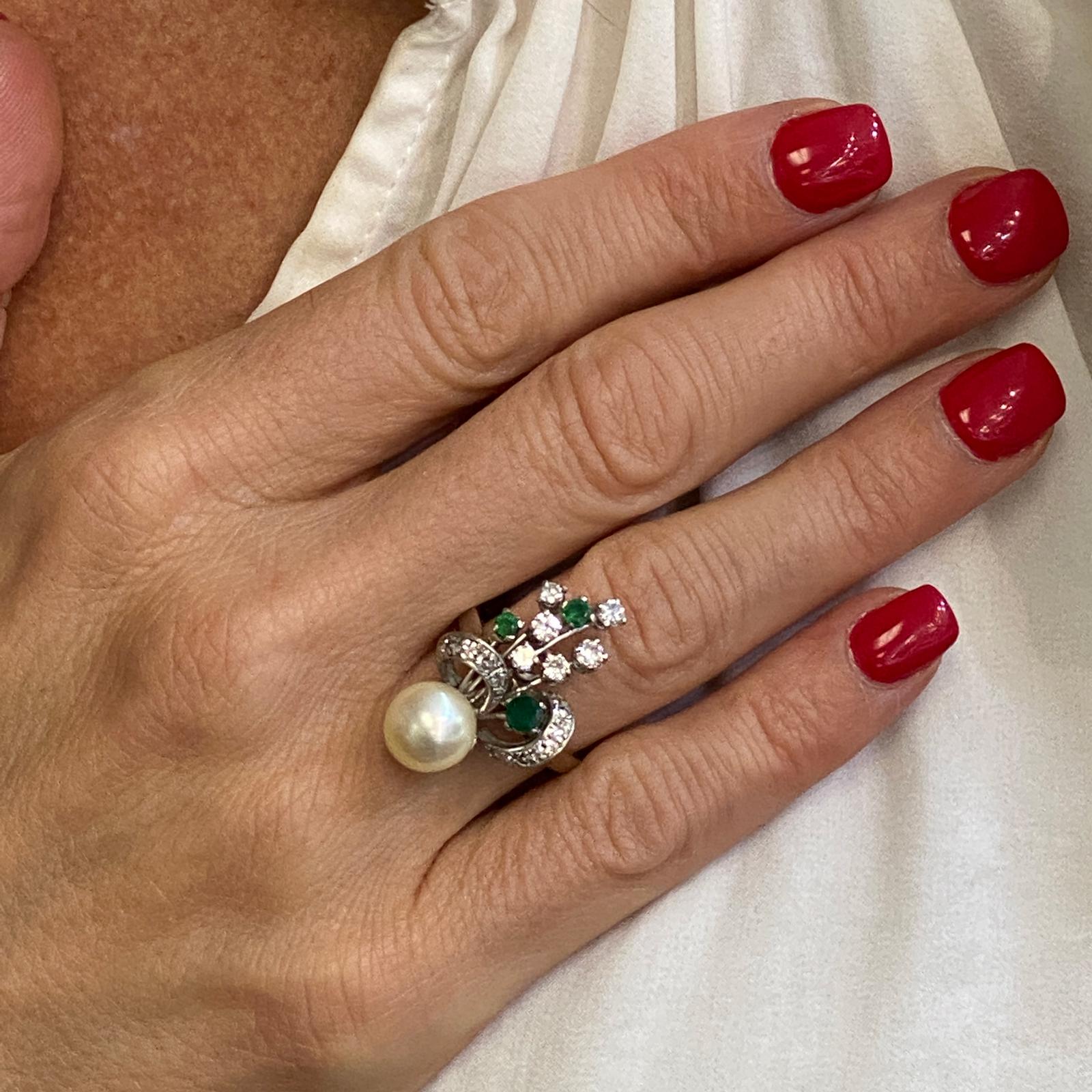 1940's diamond, emerald, and pearl vintage cocktail ring fashioned in 14 karat white gold. The ring features 20 round brilliant cut diamonds weighing .80 CTW, 3 round emeralds, and an 8.8mm cultured pearl. The top of the ring measures 15 x 28mm, and