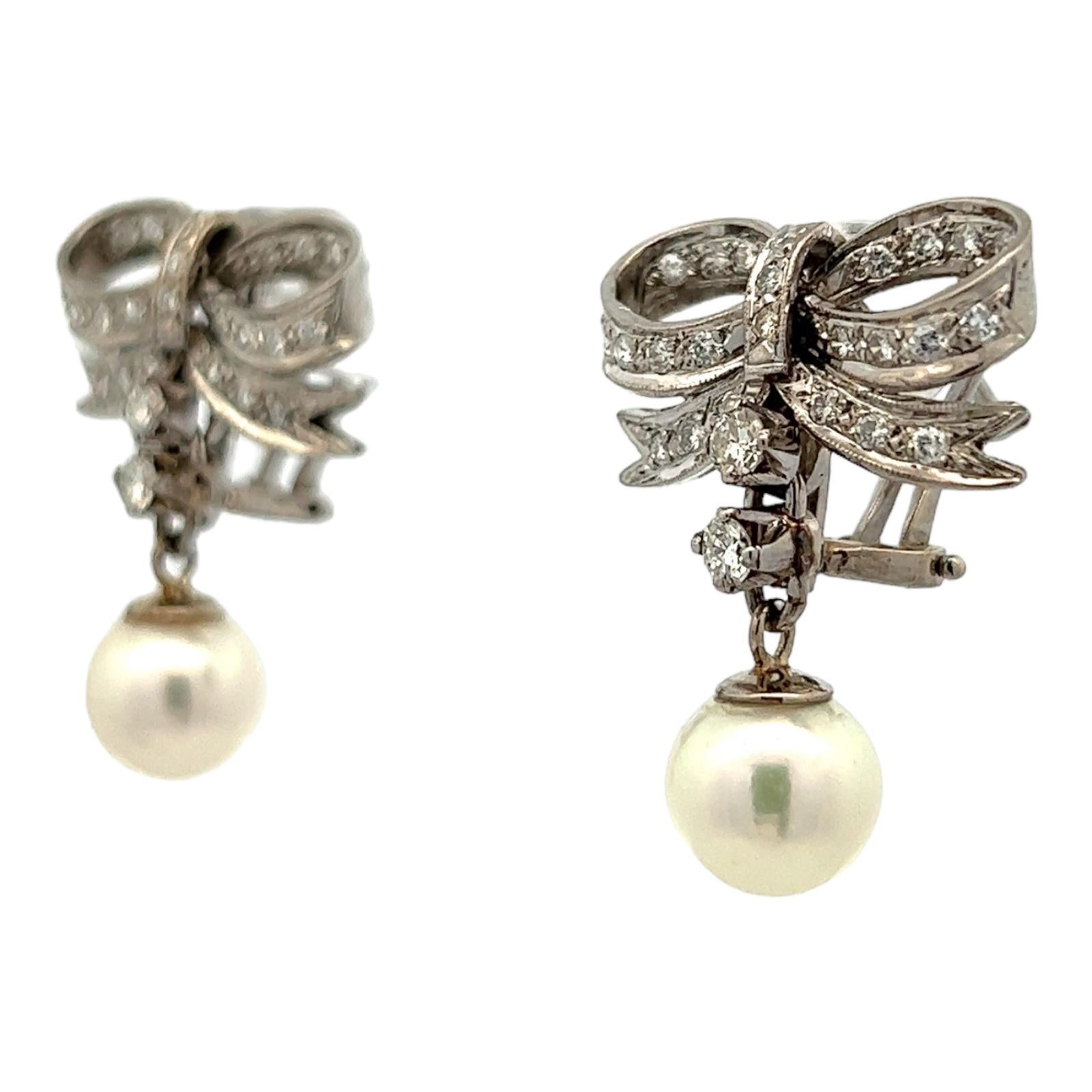 Mid 20th Century diamond ribbon earrings with cultured pearl drops are fashioned in 14 karat white gold. The ribbons feature round brilliant cut diamonds weighing approximately 1.00 CTW and graded H-I color and VS2-SI1 clarity. The earrings measure