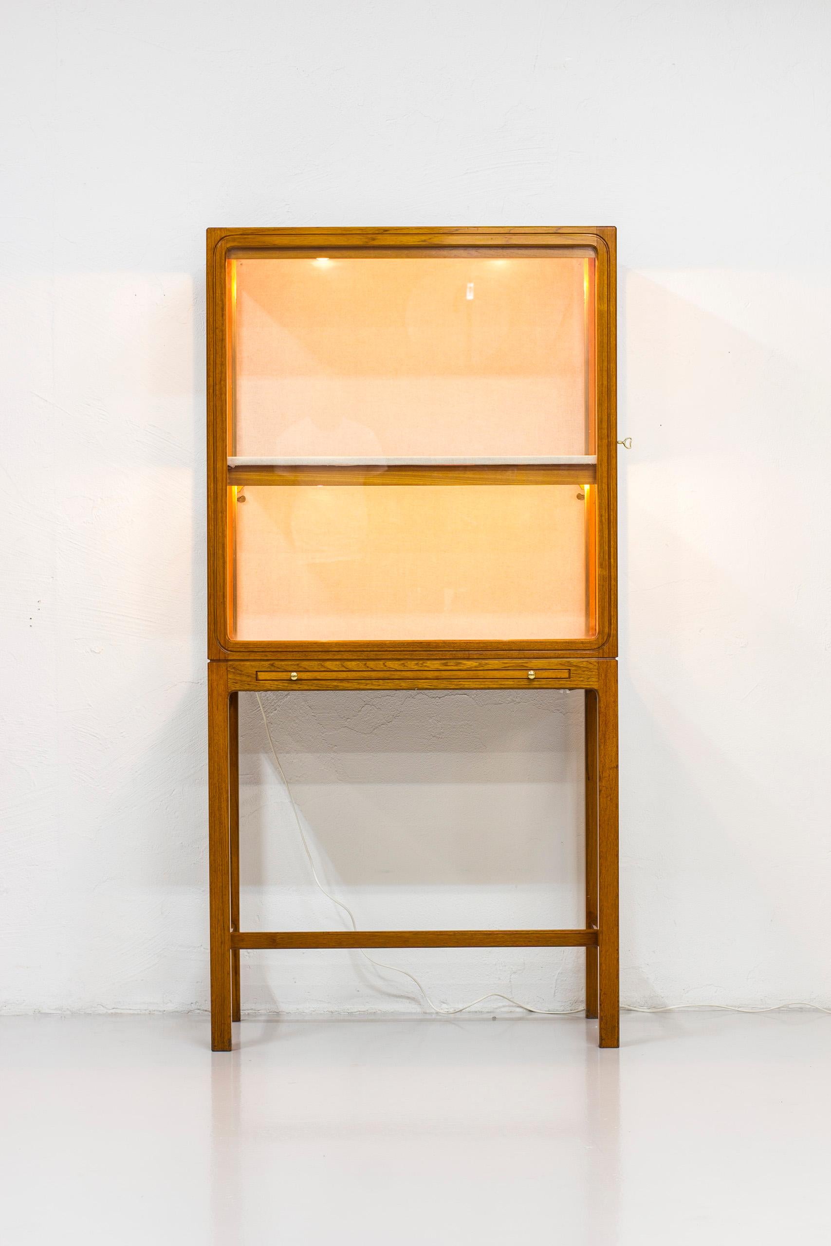 Display cabinet produced by Nordiska Kompaniet in Sweden. Likely designed by Carl-Axel Acking. Produced between the 1940-1950s. Made in solid mahogany, brass and glass. With linen upholstery in natural color on the inside. Built in display light.