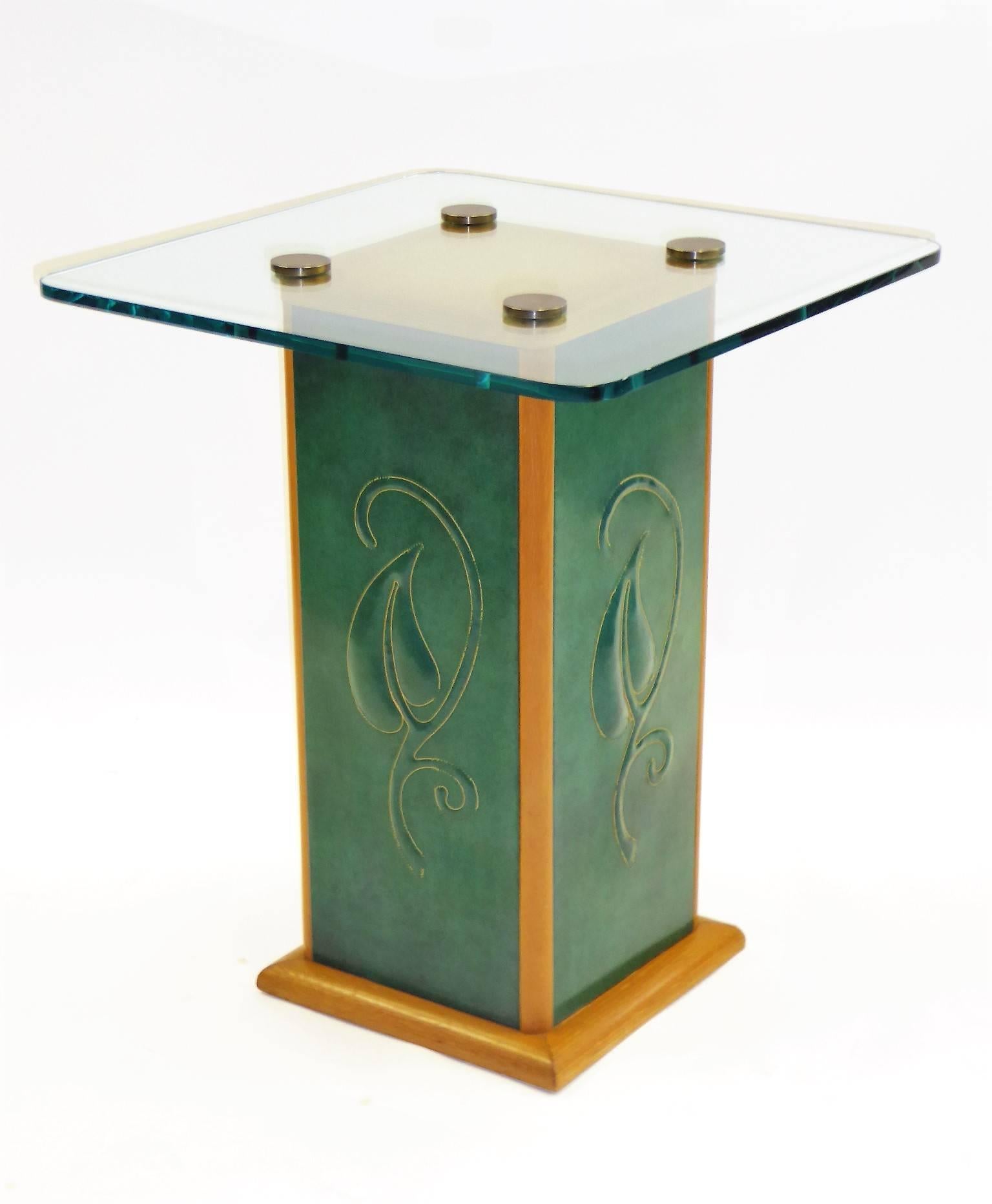 Beautiful late Streamline Moderne Edward Stoll designed table with 1/2 inch glass top over a pedestal of cerused oak and side panels of quilted green leatherette, a tropical leaf motif centered. Brass button medallions secure the glass top. In very