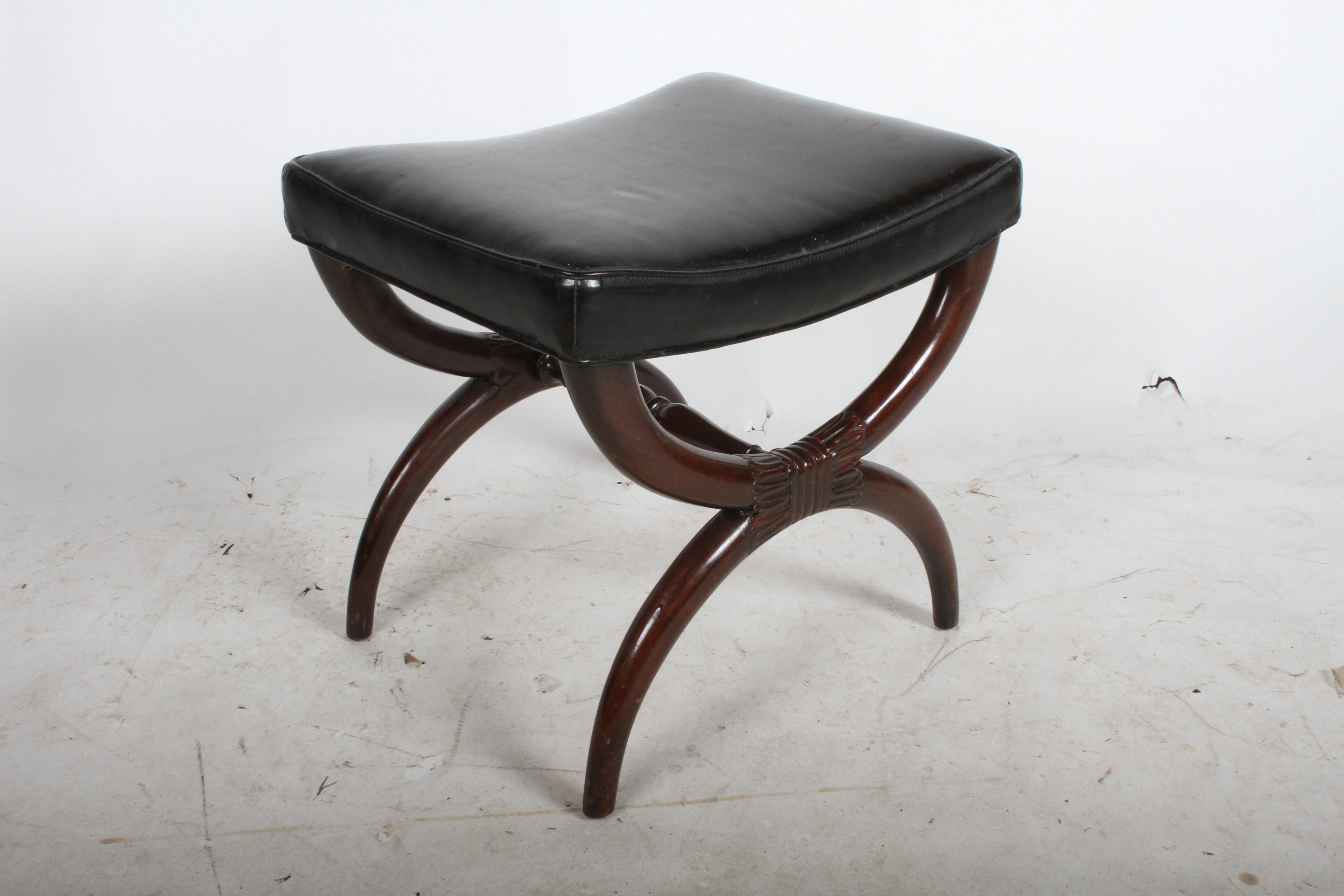 Early design for Dunbar, mahogany bench or vanity stool. X form base with neoclassical styling, and original black leather seat. Mahogany frame will be refinished prior to shipping, included in price. Black leather seat has wear, should be replaced.