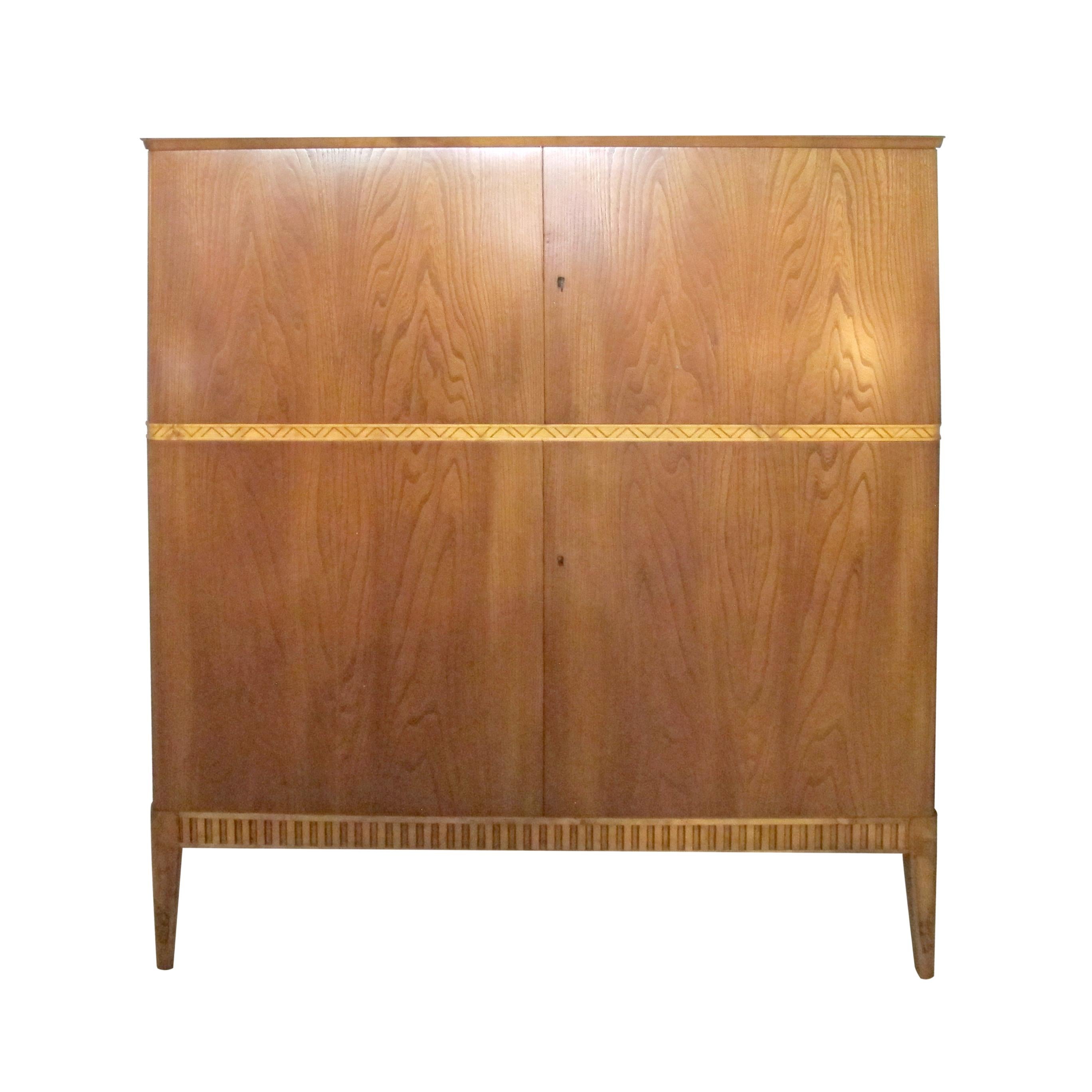 Cette armoire suédoise présente d'élégants placages de frêne, mettant en valeur le grain naturel du bois. La pièce maîtresse du design est une frise magnifiquement sculptée, qui court horizontalement à travers le milieu, ajoutant un élément