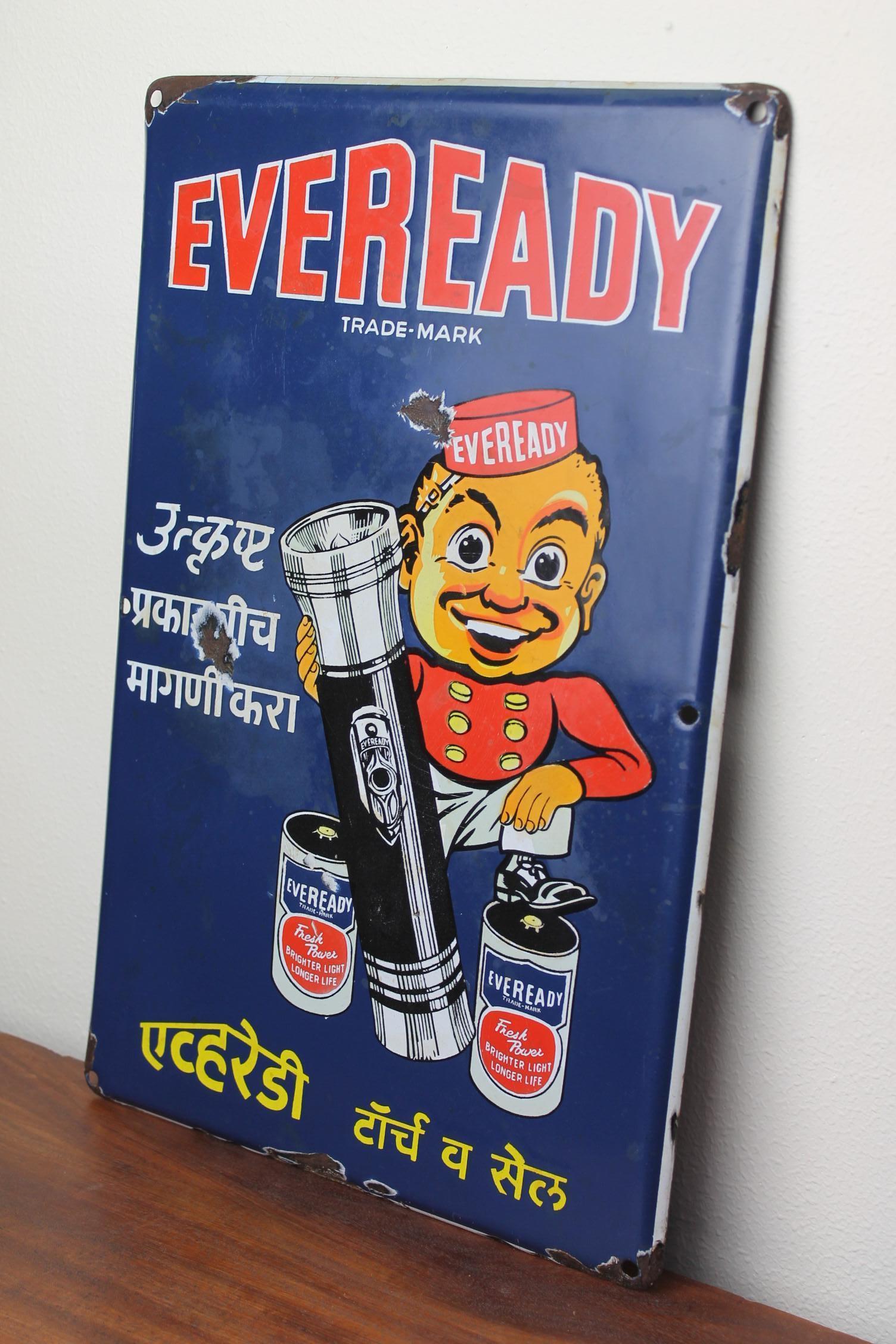 Rare enseigne en porcelaine vintage à collectionner, enseigne en émail, enseigne publicitaire émaillée, art publicitaire ancien pour les piles Eveready.
Ce présentoir publicitaire montre un garçon Piccolo - Bell, avec deux piles et une lampe de