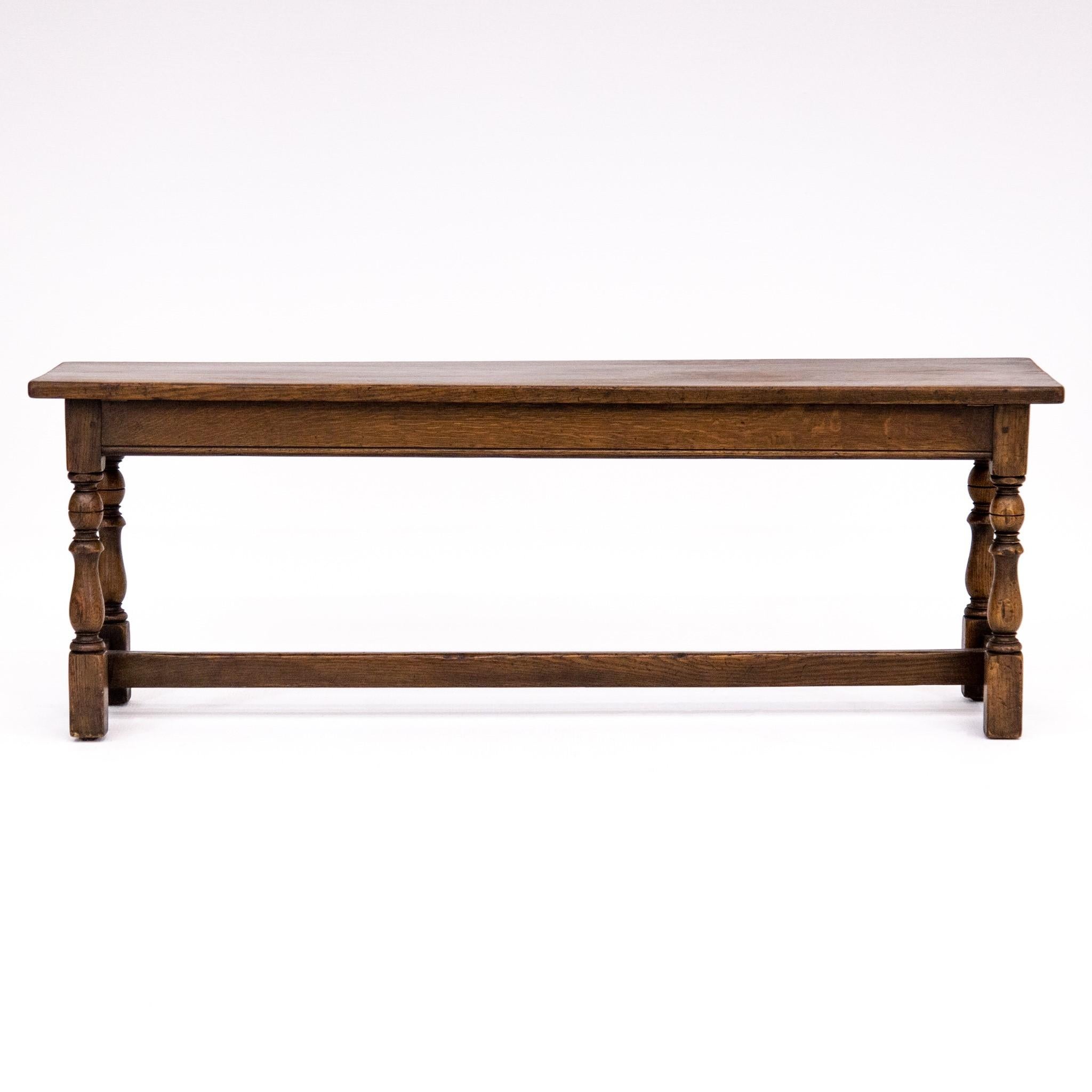 Traditional William & Mary-style long narrow oak bench made in England for Carson Pirie Scott, circa 1940s. It serves as a very versatile decorating piece featuring turned and block legs joined by a low H stretcher. The original antiqued finish is