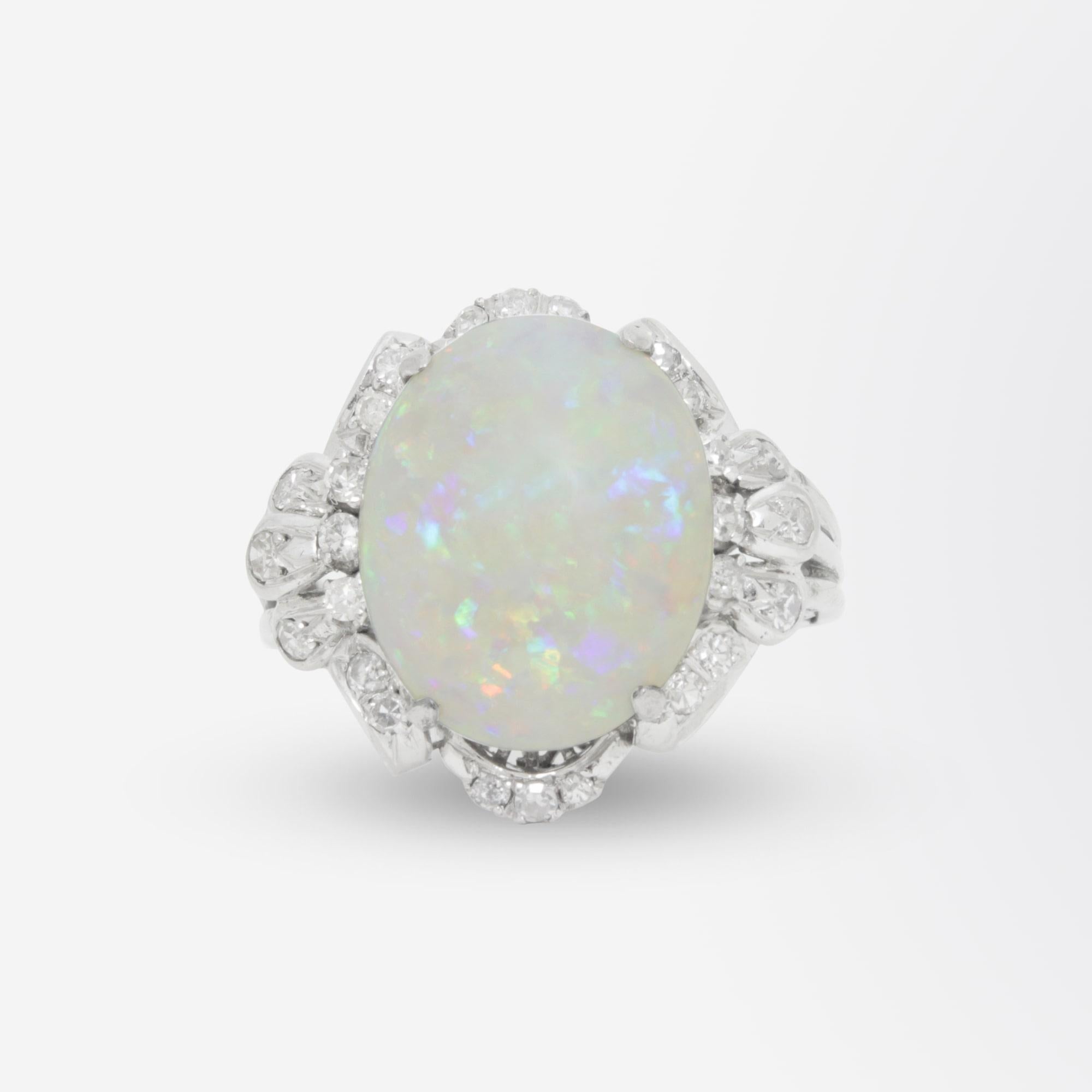 A fine late Art Deco period cocktail ring crafted from 18 karat white gold. The 27 stone ring is set with a central 6 carat oval cabochon cut white opal. The opal grades as 'white with mixed floral rolling pattern of red blue green violet flash' and