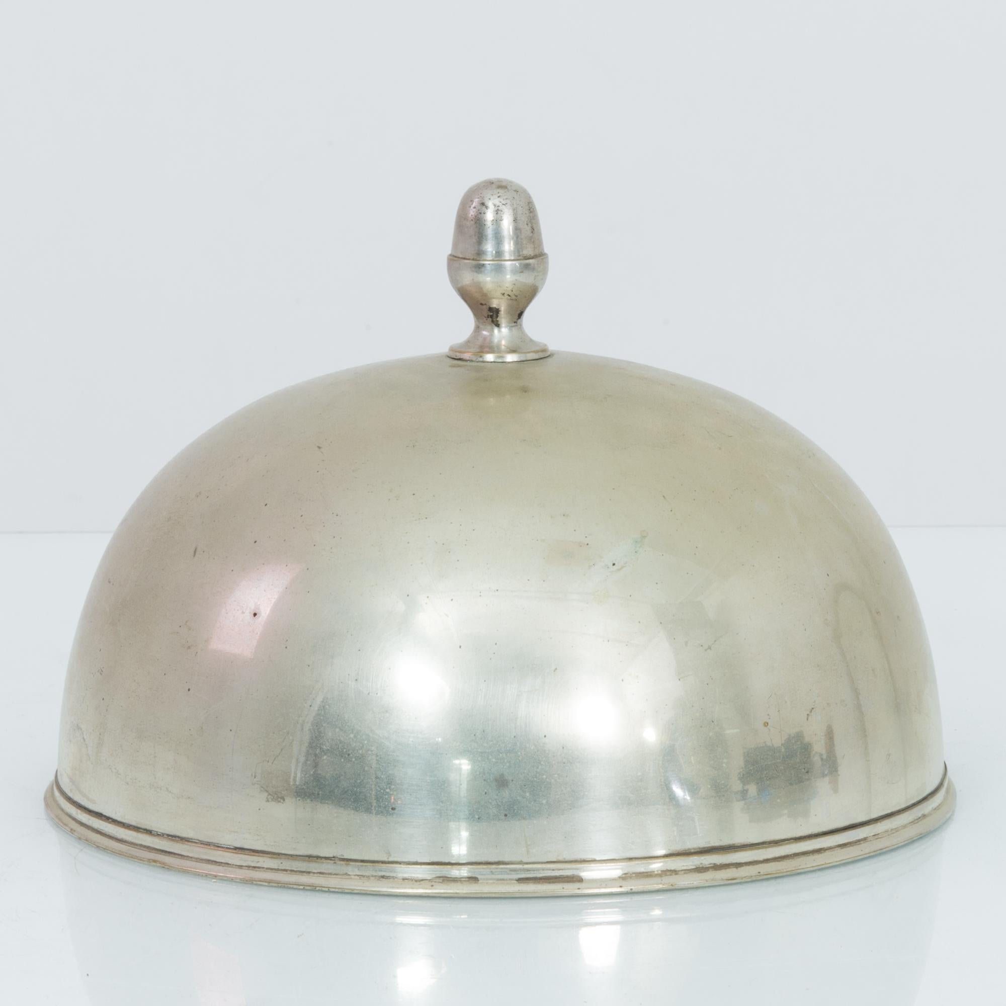 This silver-plated serving cloche was made in Europe in the 1940s. Gracefully decorated with a carved rim and a globe finial on the lid. Its timeworn patina imparts an elegance from yesteryear.