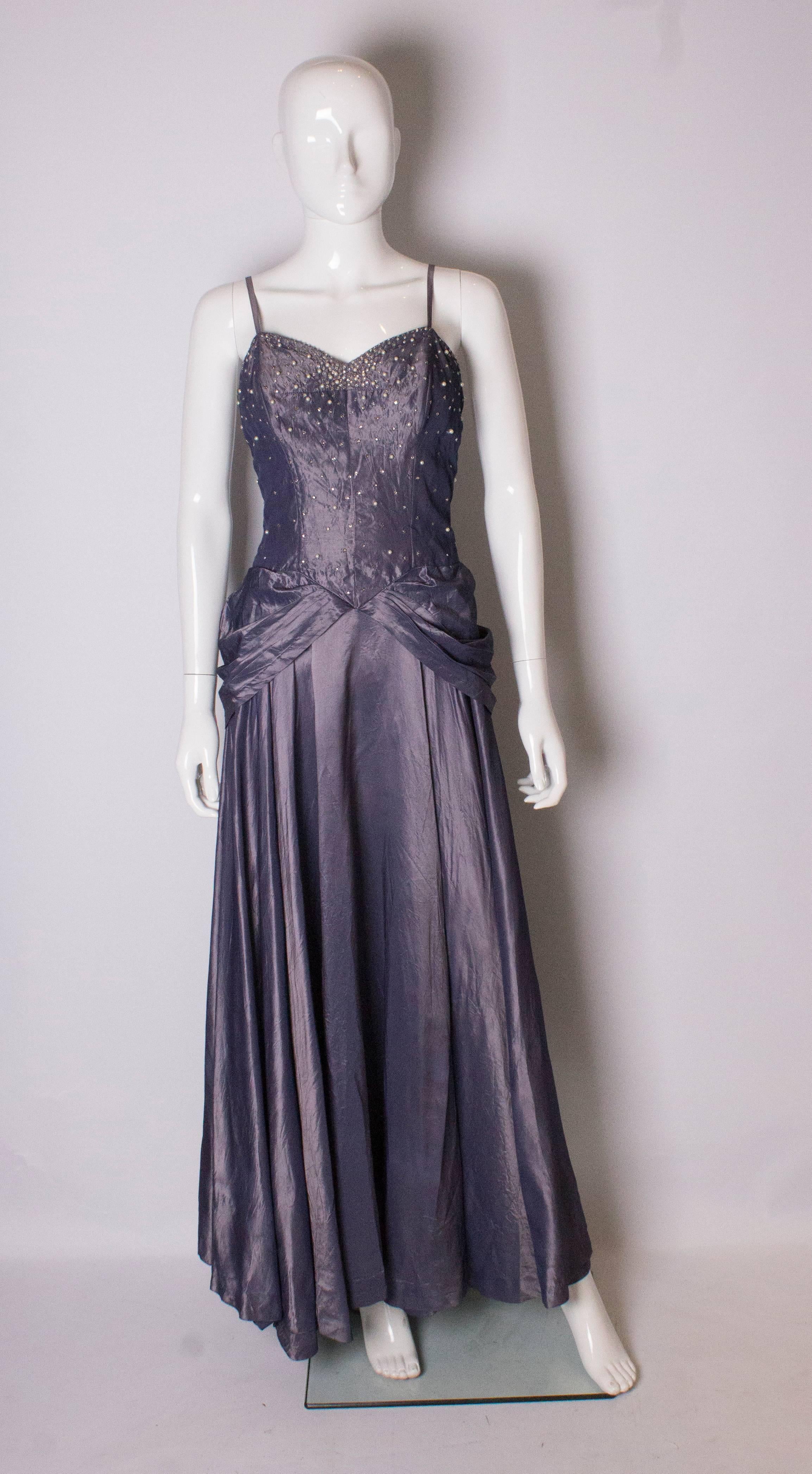 A pretty  1940s gown by Robert Goldberg. The gown is in a dusty lilac colour with spagetti straps and pearl and diamante detail on the bust area. It has a central back zip and full skirt, with sash detail at the waist.